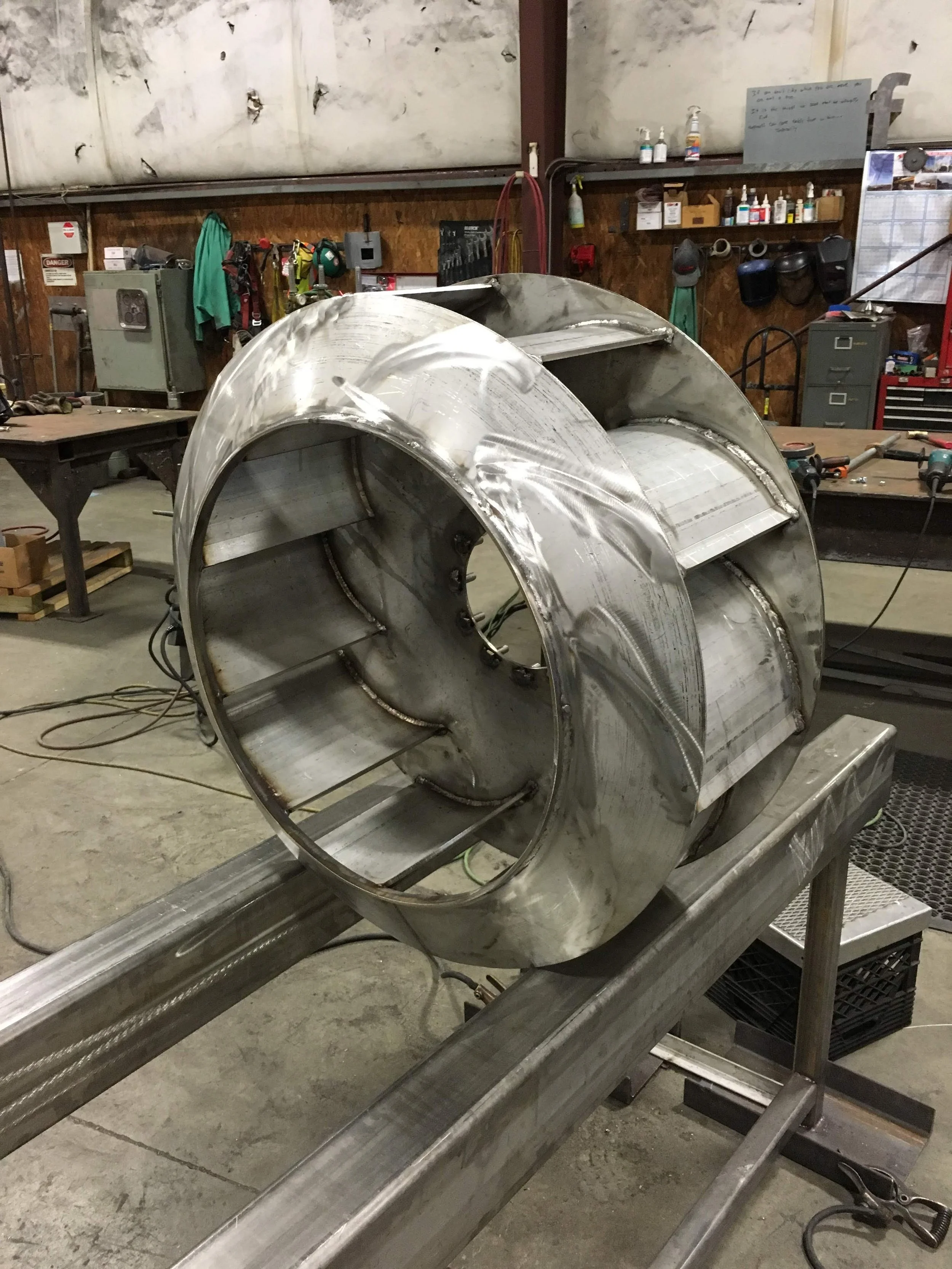 A large metal cylindrical object on a workbench in a workshop, surrounded by tools and equipment.