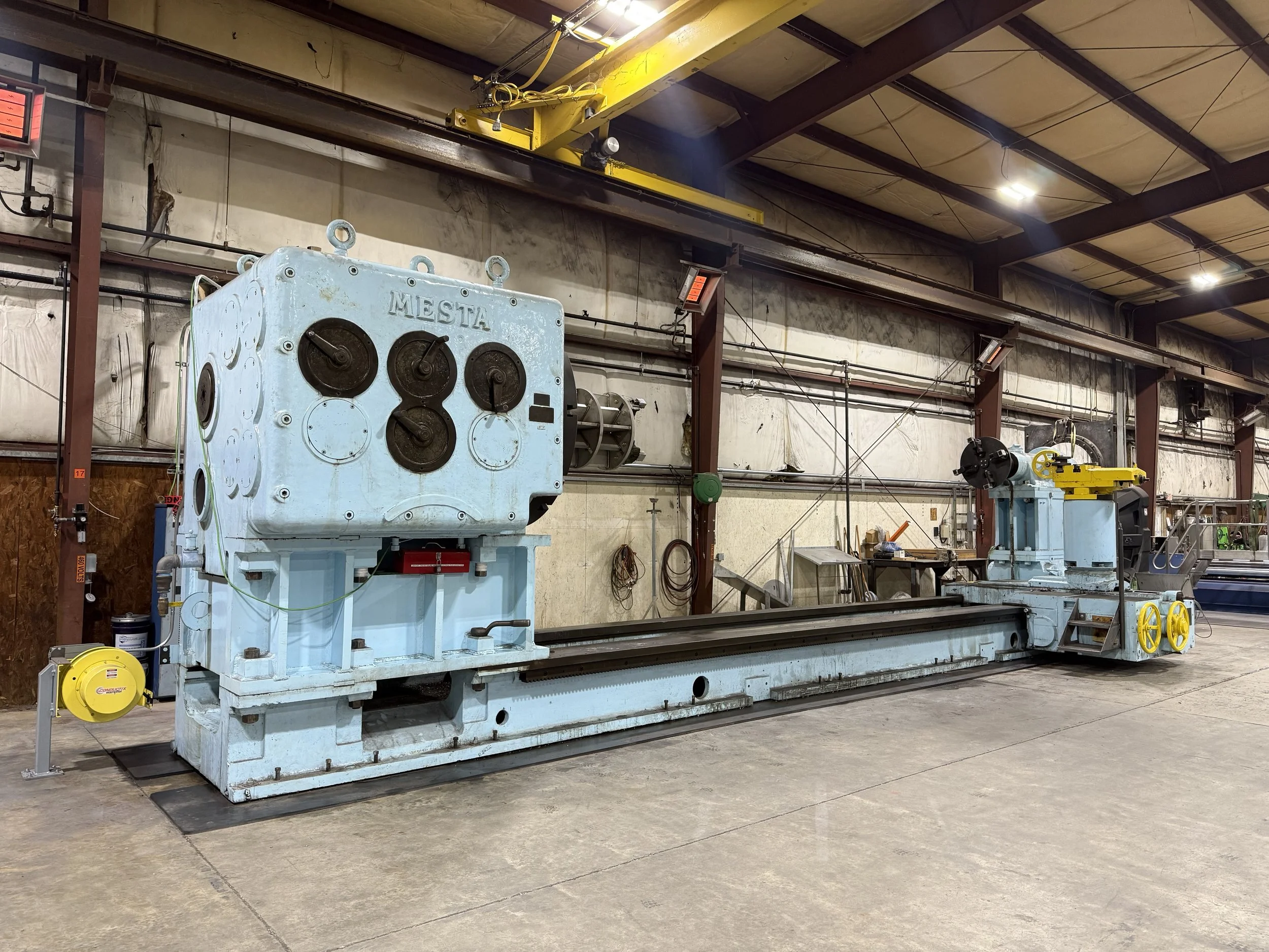 Large blue industrial machine with multiple control dials and a long horizontal guide rail inside a warehouse or factory setting.