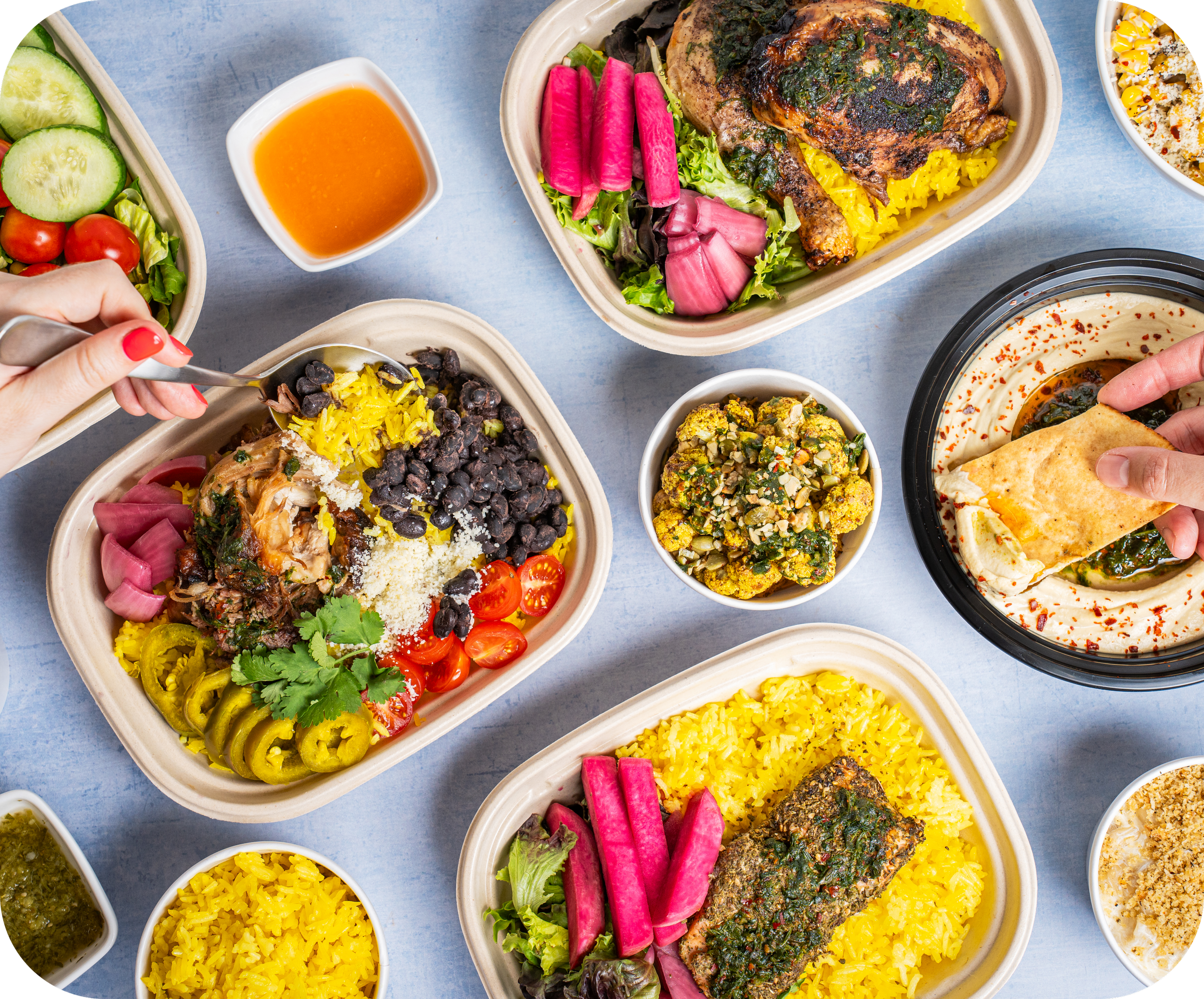 An assortment of Middle Eastern food containers on a light blue table, including rice, salads, grilled meats, hummus, and various garnishes.