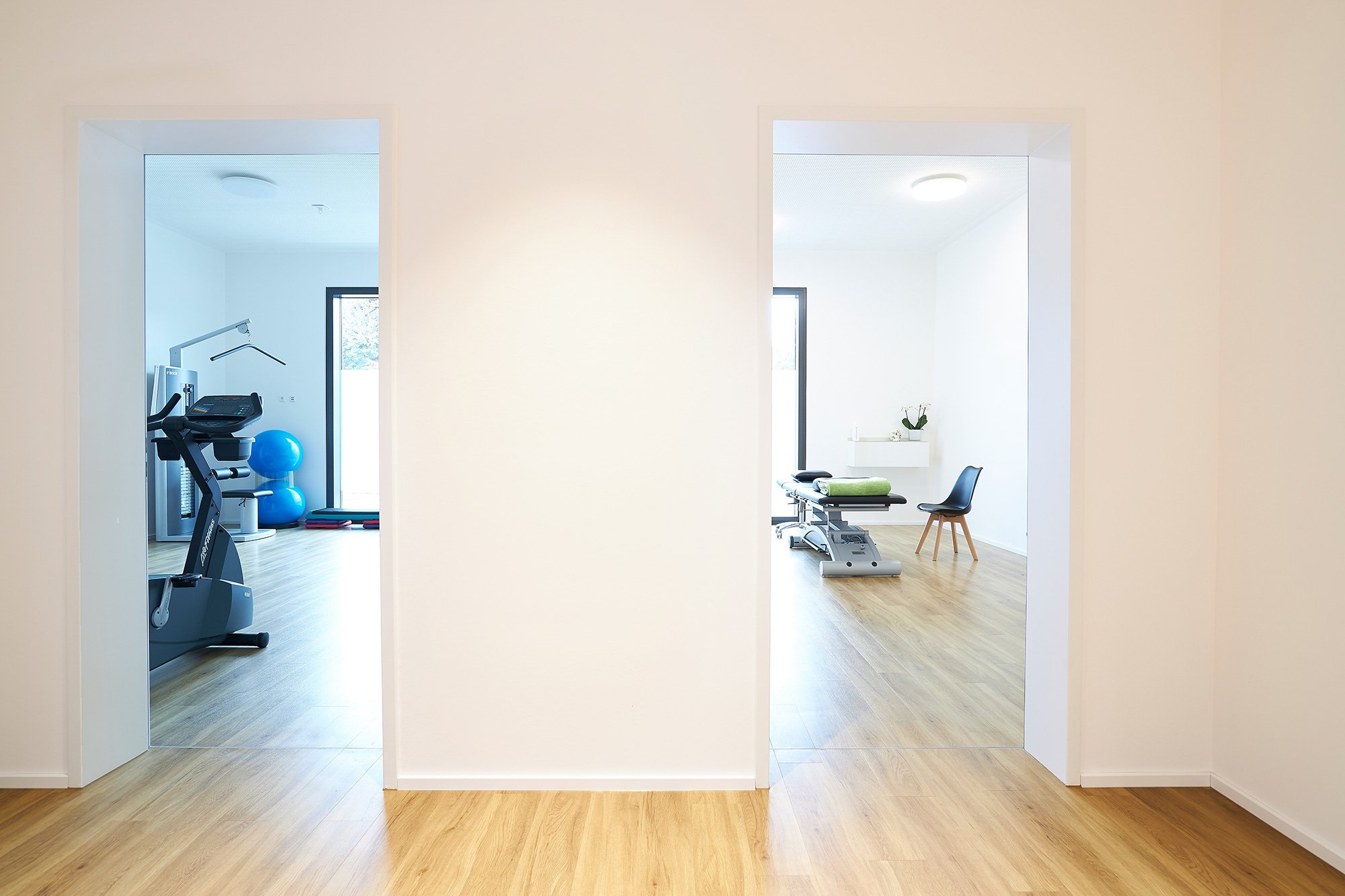 Zwei Behandlungsräume in einer medizinischen Einrichtung, jeder mit Behandlungsliegen, Stühlen und medizinischer Ausstattung, klar und hell beleuchtet, mit Holzboden.