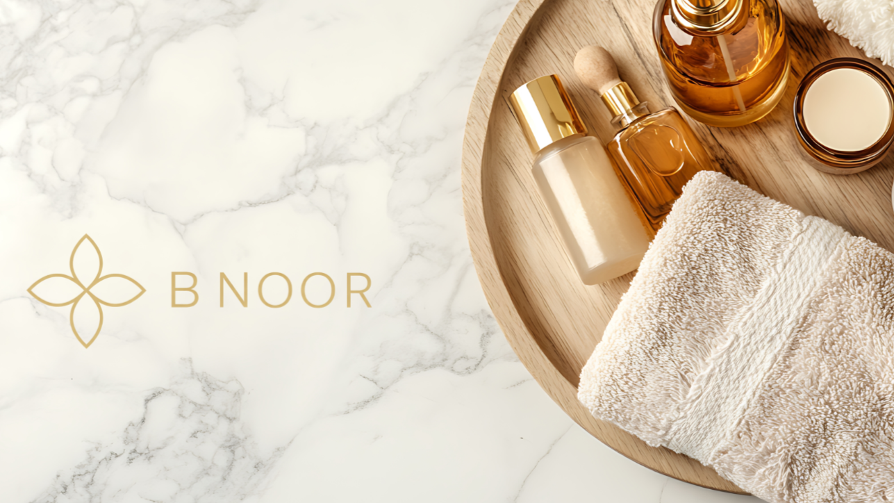 A wooden tray holding skincare products, a beige towel, and a marble surface background with a gold logo reading 'B NOOR'.