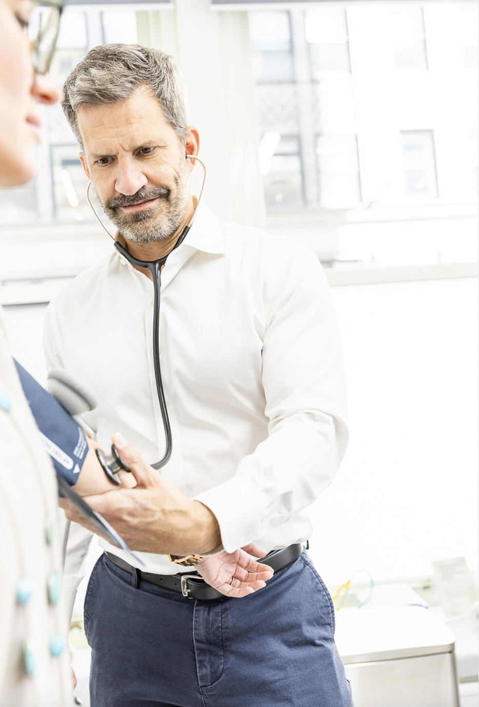 A male healthcare professional using a stethoscope on a patient in a bright clinic or hospital setting.