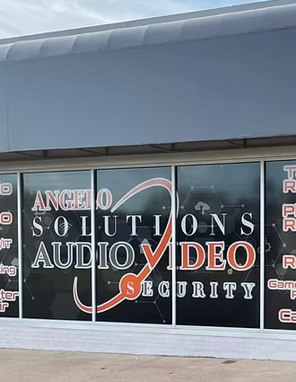 Storefront window advertisement for Angelo Solutions, specializing in audio and video security, with text and graphics on the glass