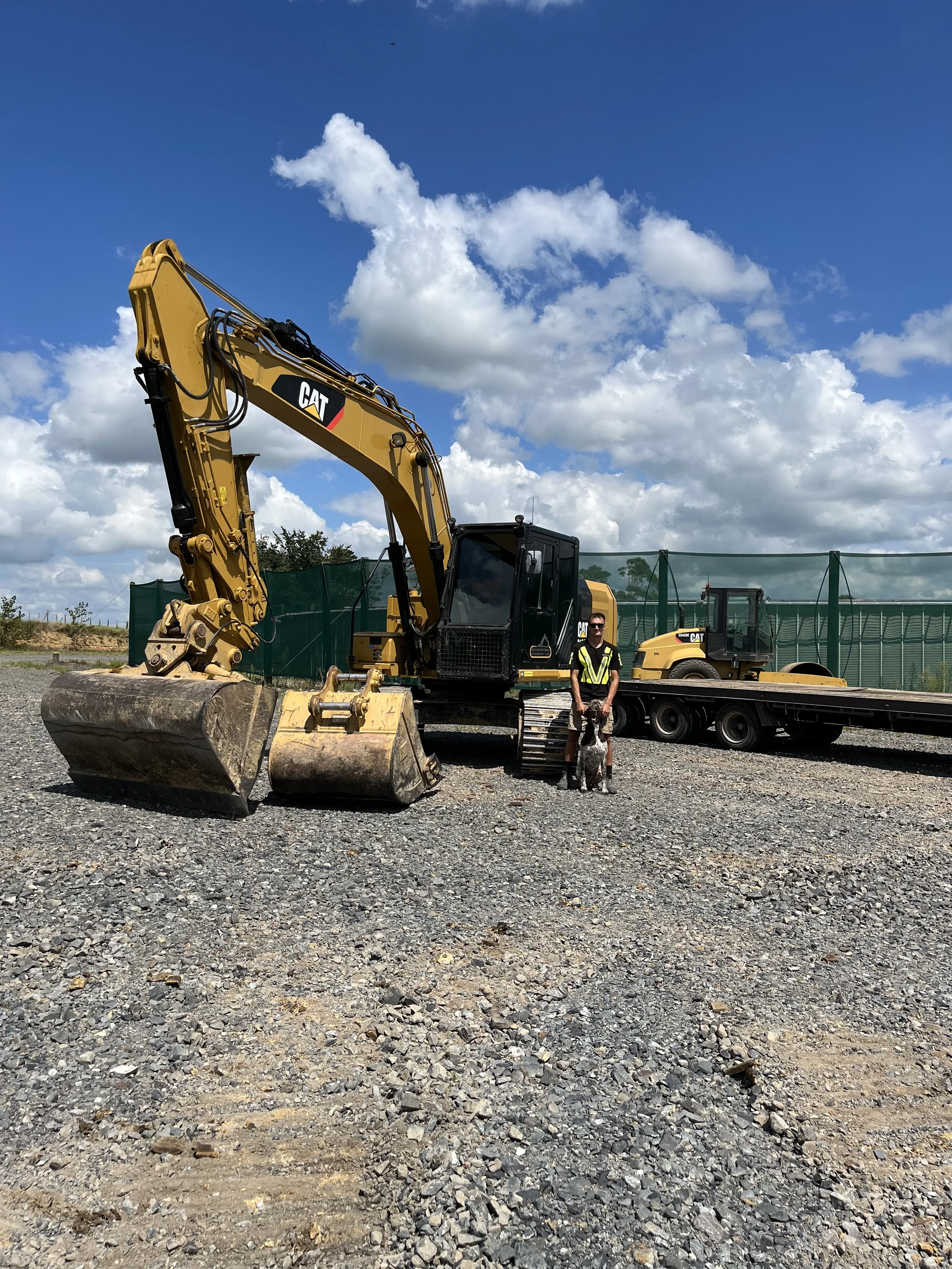 A construction site with a yellow CAT excavator, roller and large transporter truck.
