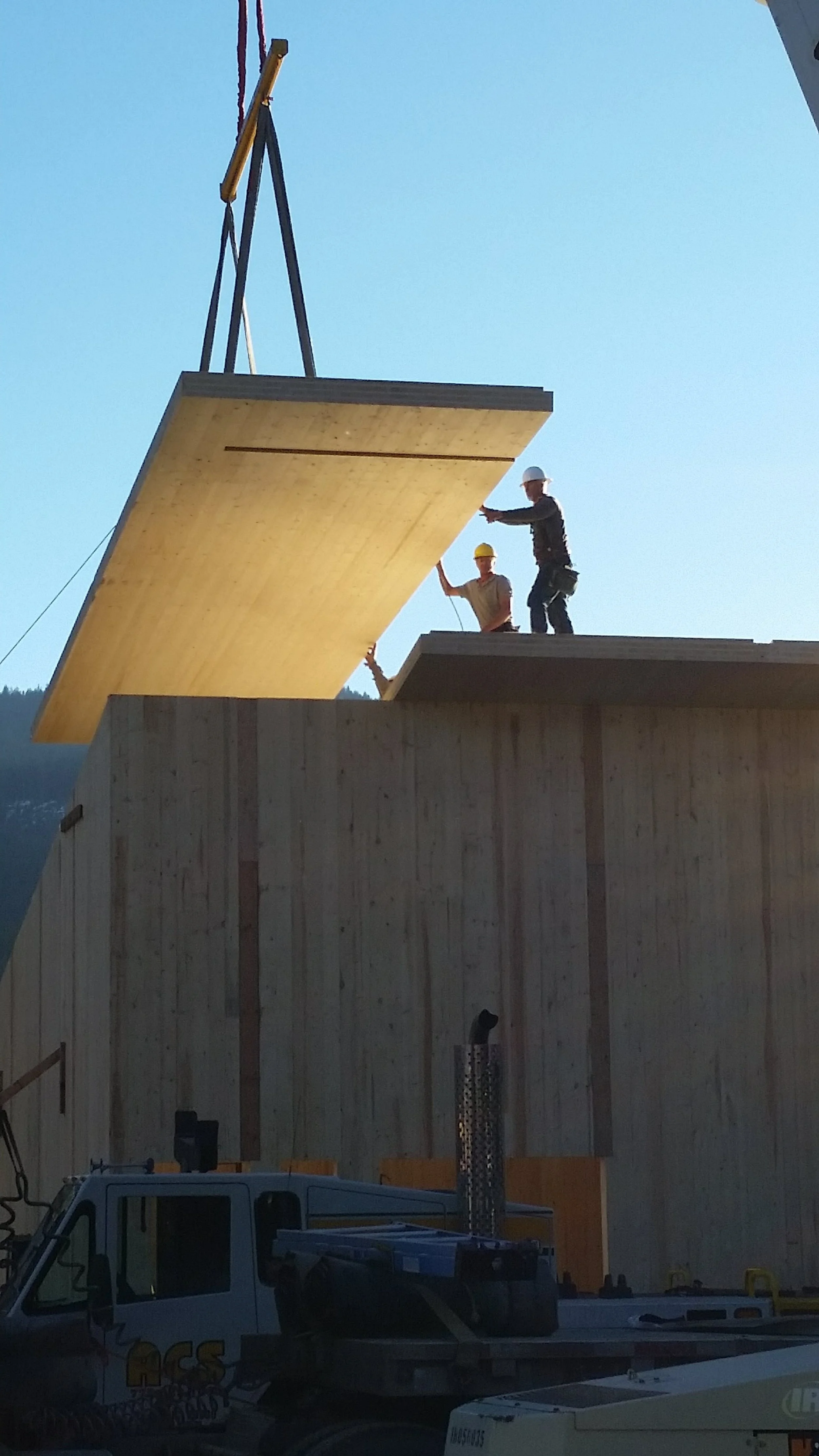 Construction workers installing large wooden CLT panels on a building under construction, with a crane lifting a panel into place.