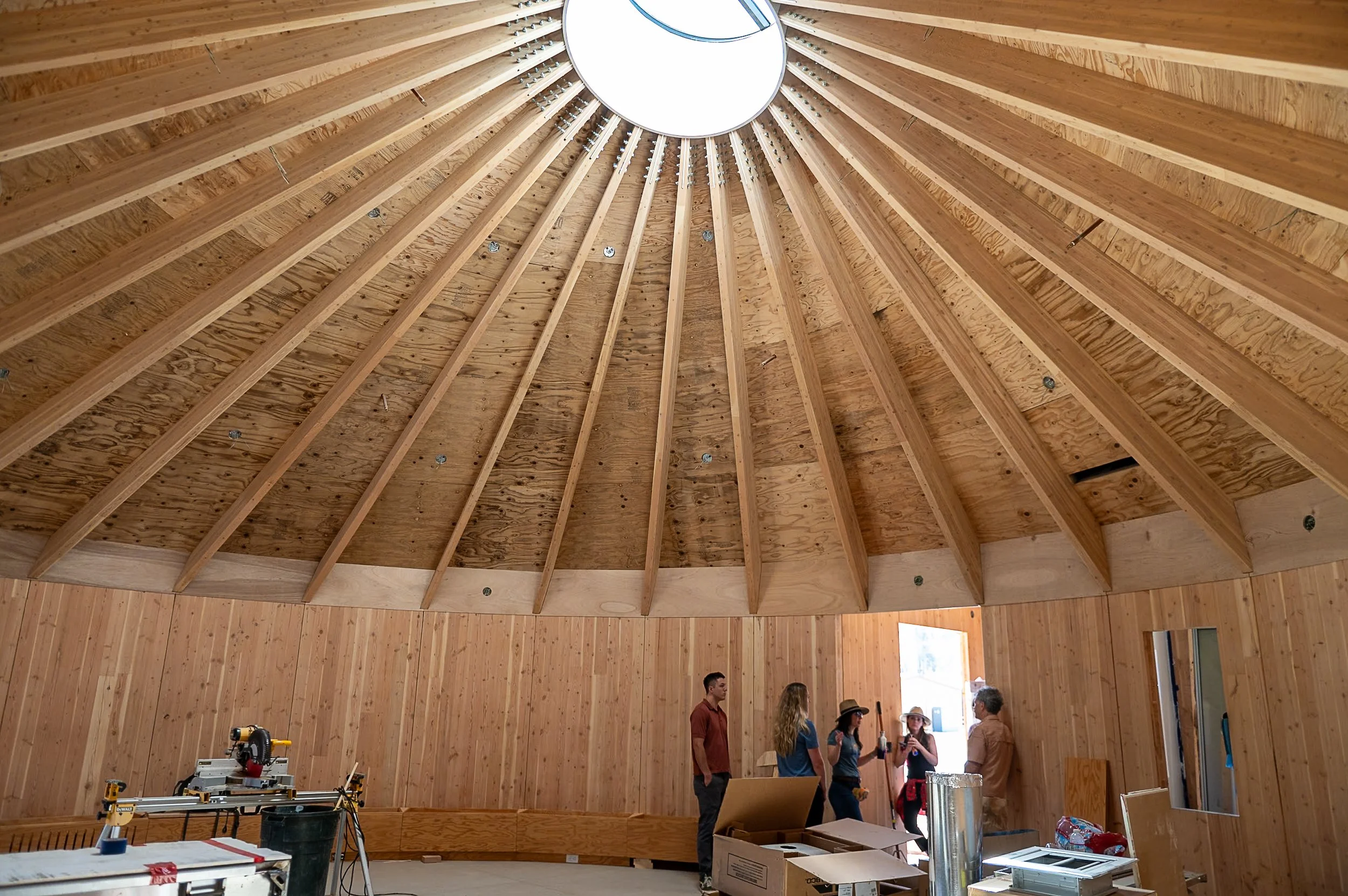 Interior of Roundhouse Council Building in Greenville, CA. A wooden CLT dome structure with people inside, construction tools, and materials present.
