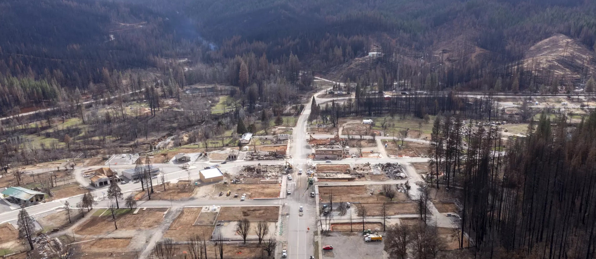 Aerial view of a Greenville, Ca after the Dixie Fire of 2021 with trees, roads, and some buildings, showing damage and debris from a recent fire or disaster.