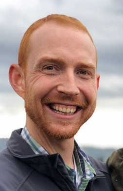Levi Huffman, Close-up of a smiling man with red hair and beard outdoors on cloudy day.