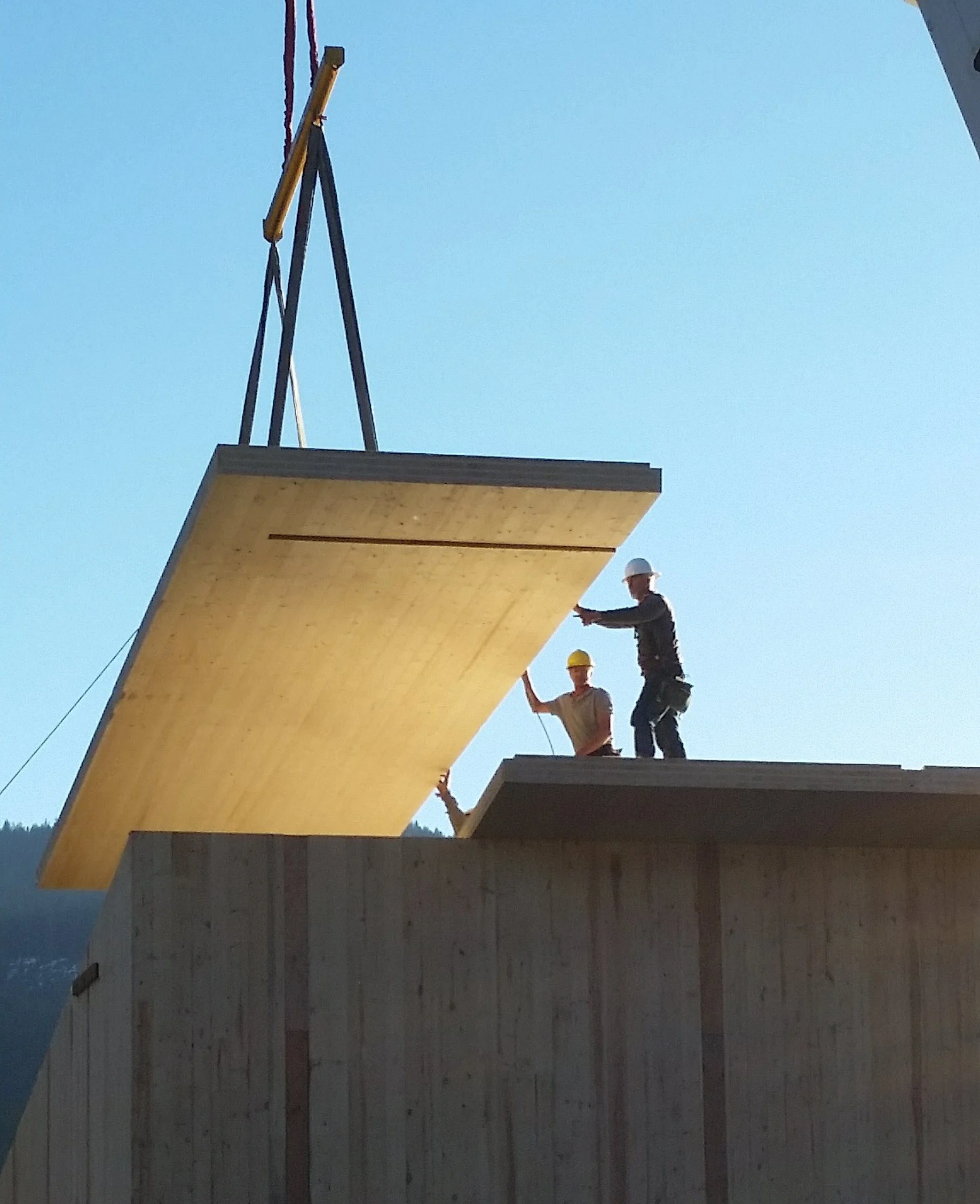 Construction workers installing a large wooden CLT panel on a building.