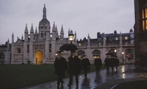 People walking with umbrellas near a historic building during rainy weather