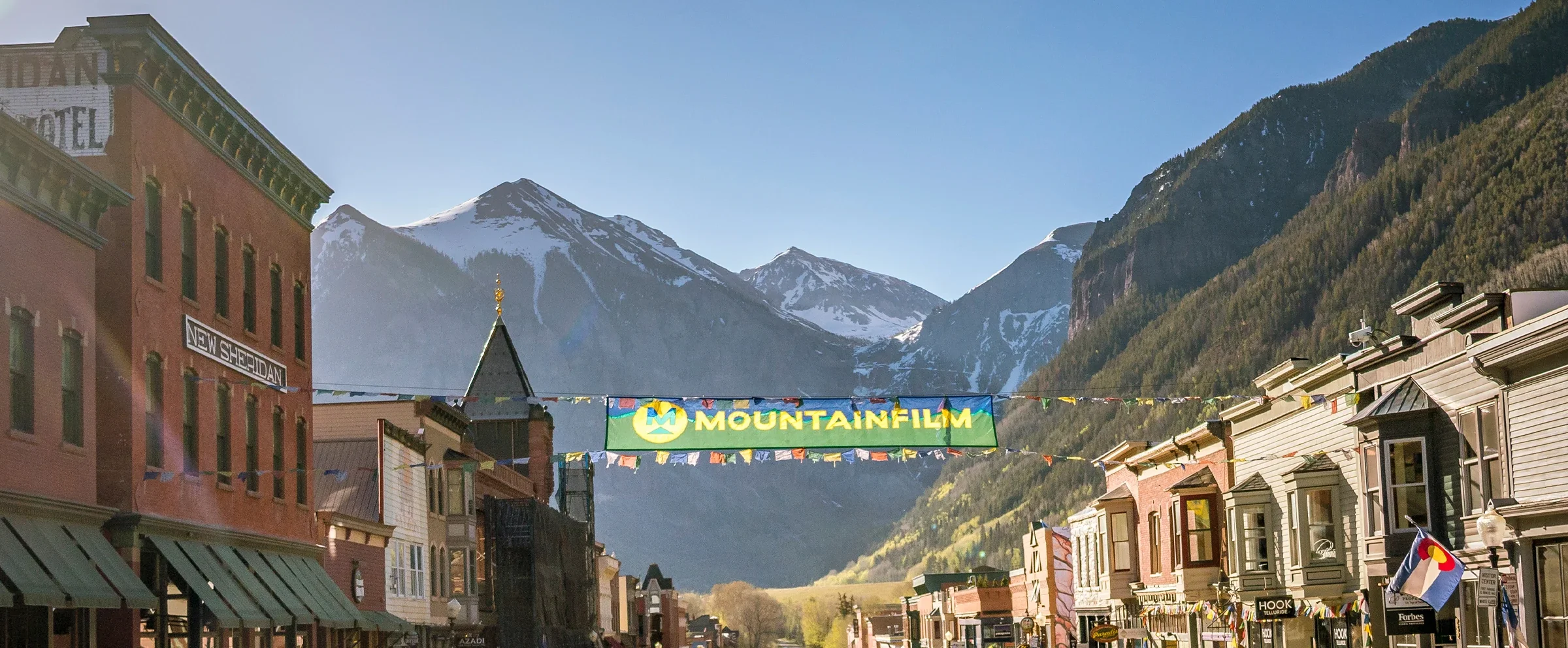 Main street in a mountain town with buildings, a sign for Mountainfilm, and snow-capped mountains in the background.