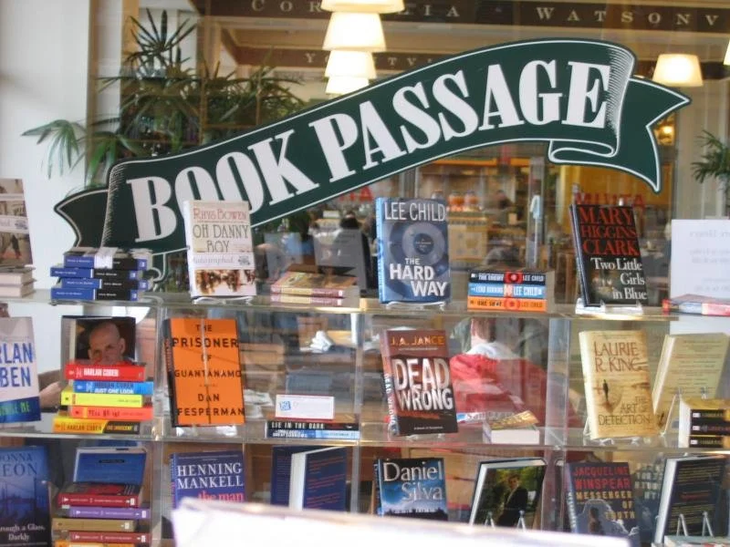 Book Passage bookstore display with books on shelves and a sign reading 'Book Passage' on top.