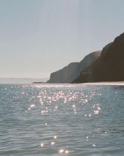 Sunlight reflecting off calm ocean waters near a rugged coastal cliff at sunset.