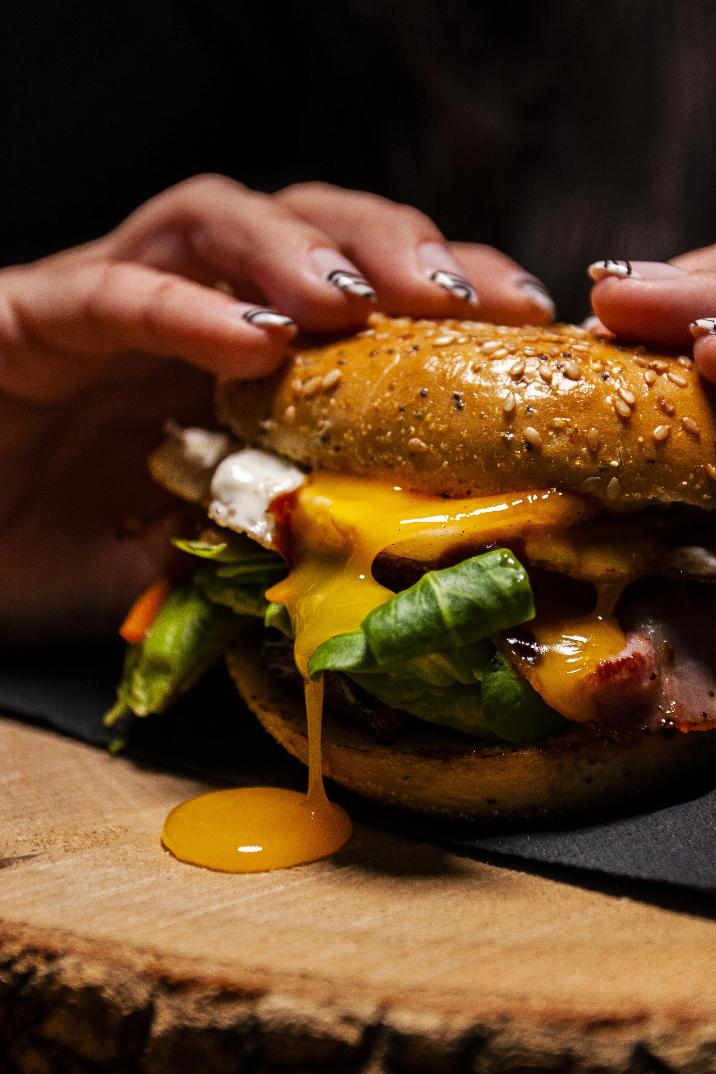 Mano colocando un sándwich con huevo frito, lechuga, tocino y pan con semillas. Contenido de redes sociales.