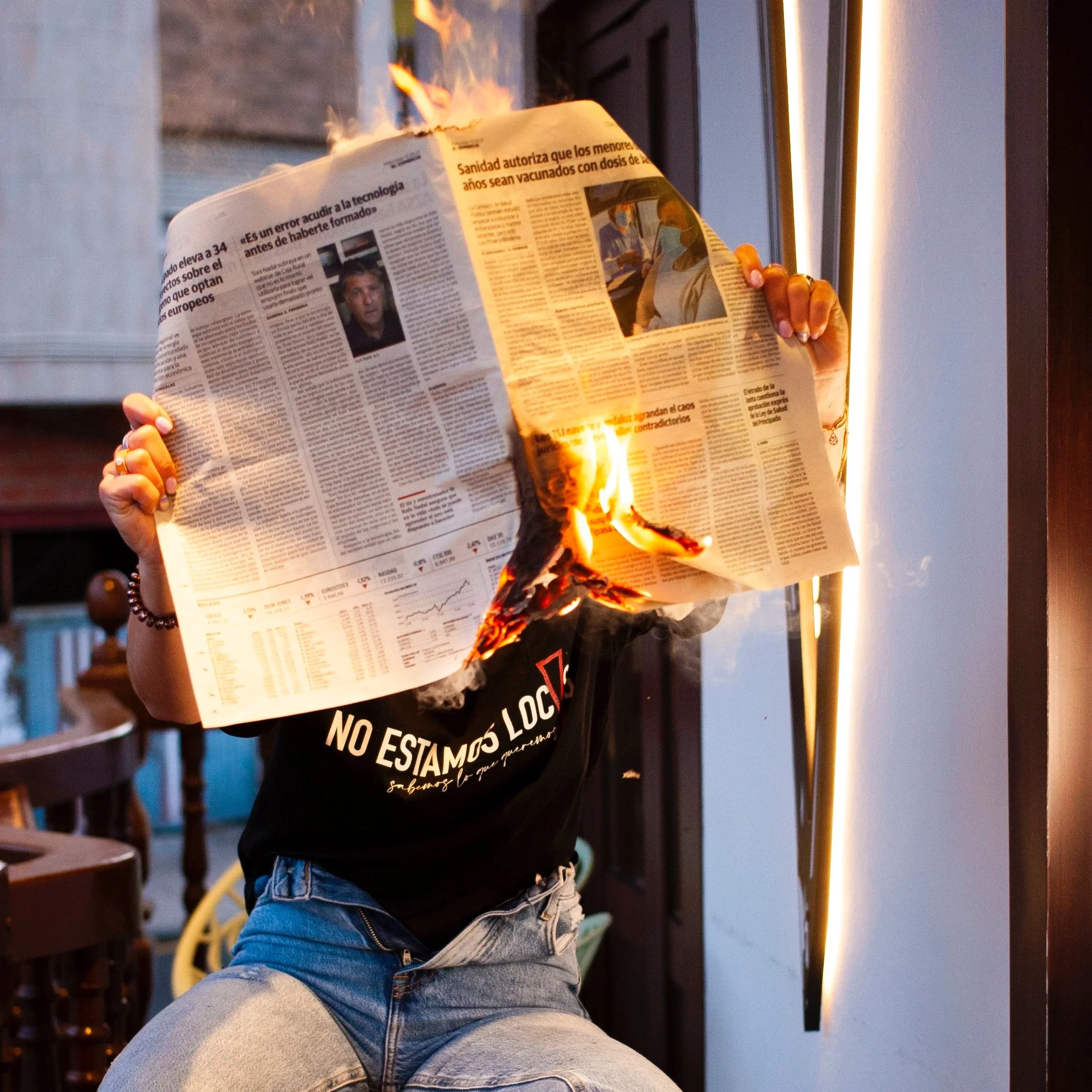 Persona quemando un periódico en un interior con iluminación cálida. Contenido de redes sociales.