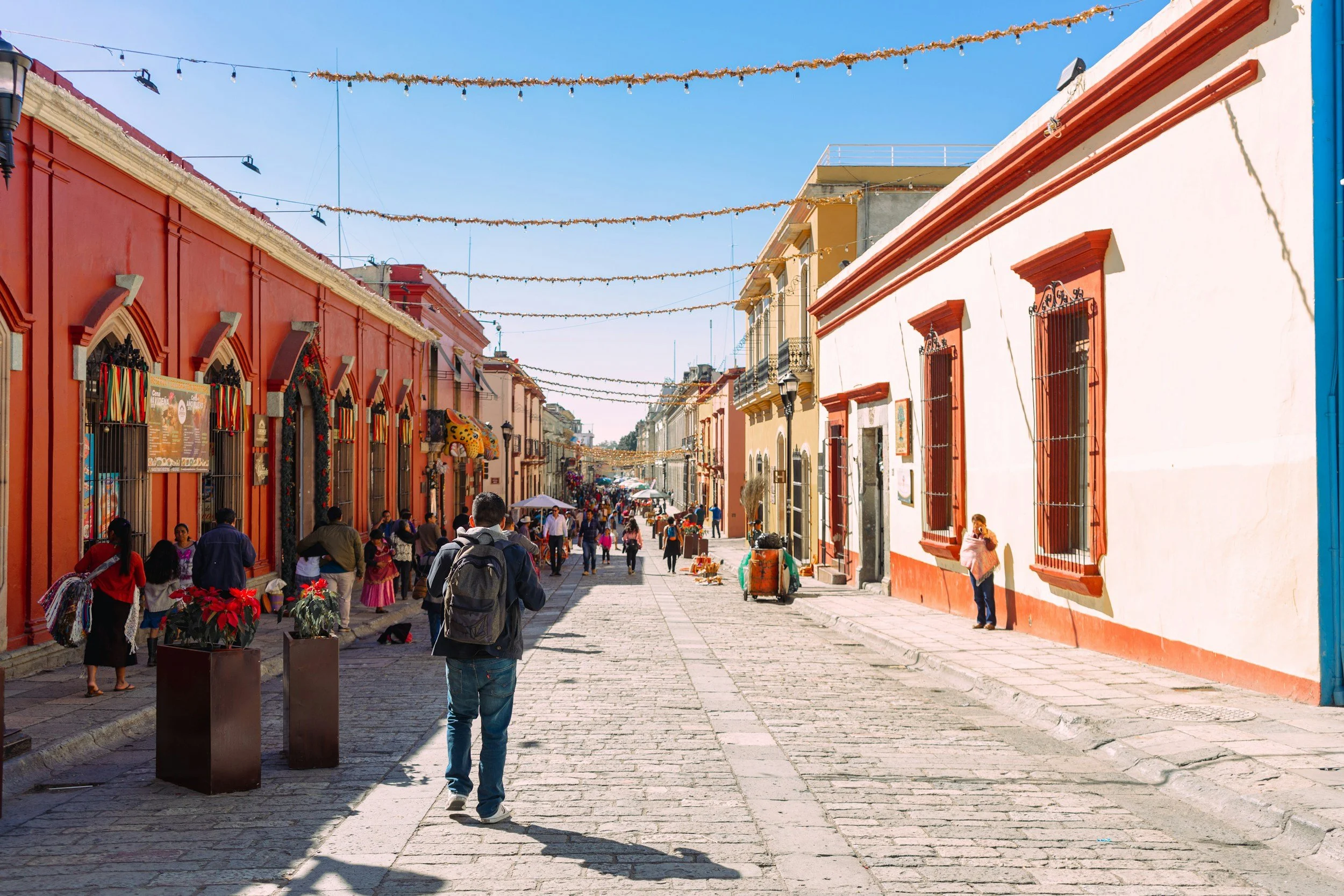 Street scene with colorful buildings, people walking, and decorations overhead on a sunny day.