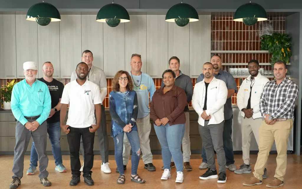 Group of 13 diverse people posing in a modern kitchen with pendant lights.