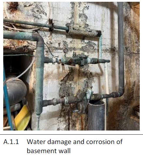 Water pipes and a valve attached to a basement wall with visible signs of water damage and corrosion.