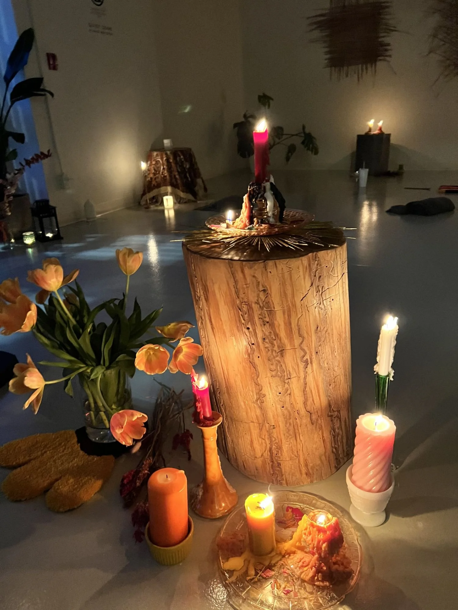 Candlelit altar with candles, flowers, and a wooden log as centerpiece, arranged on the floor for a spiritual or ceremonial setting.