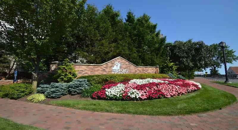 Entrance sign with floral landscaping, brick wall, trees, and a sidewalk in a park-like setting.