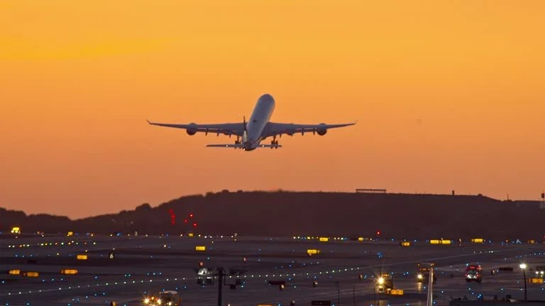 An airplane taking off from an airport runway during sunset with a clear sky.