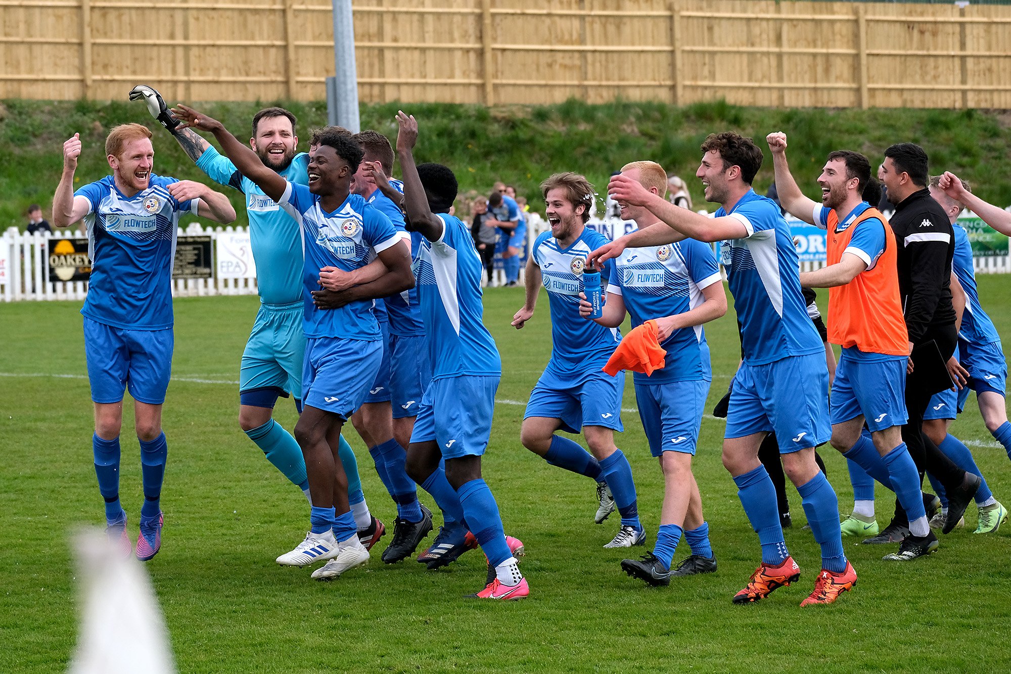 A soccer team in blue uniforms celebrating on the field, with some players jumping and others smiling and clapping.