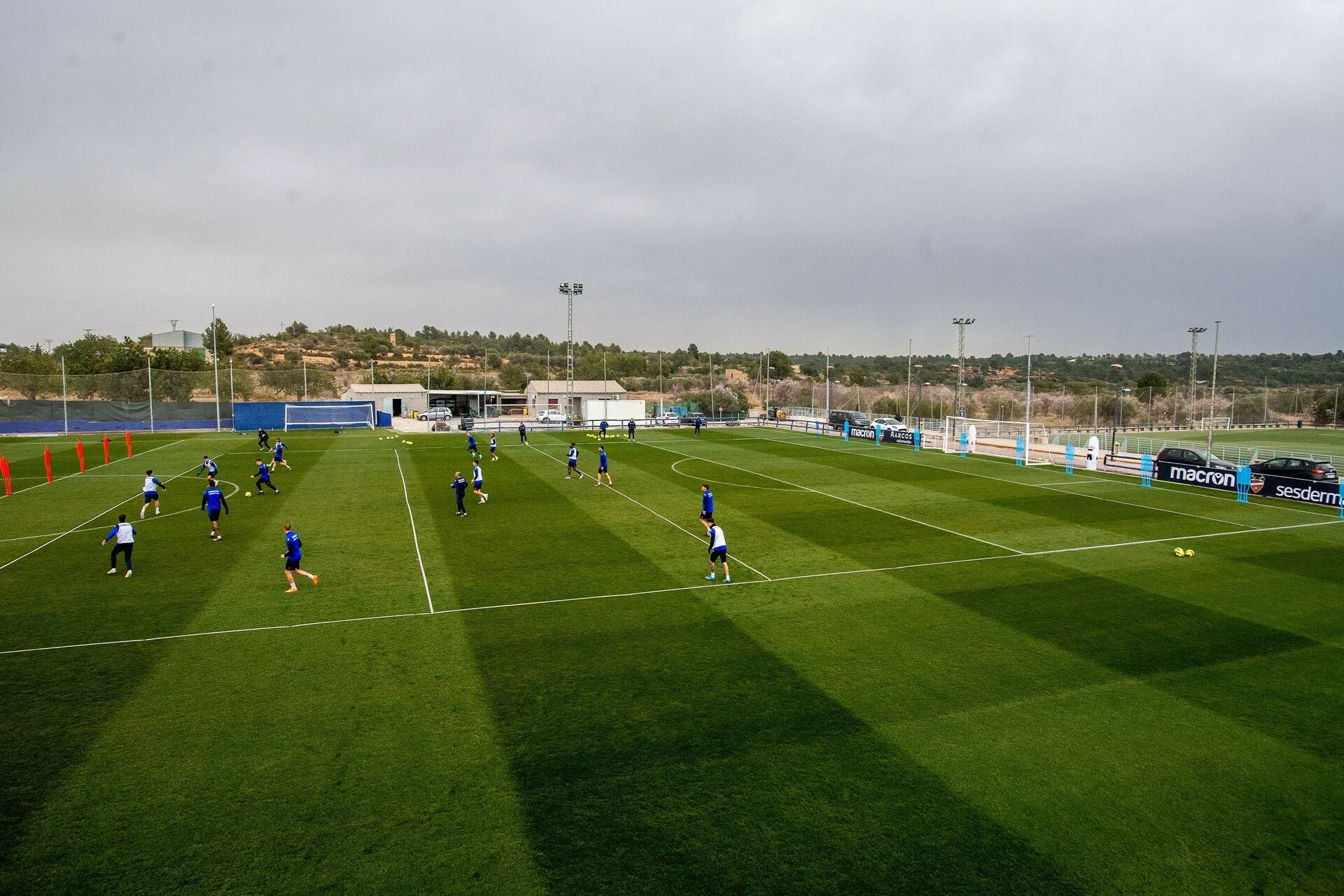 Soccer players in blue and white training on a green field under cloudy sky during practice.