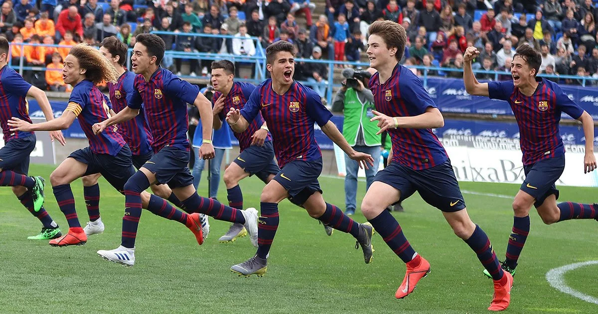 Young soccer players in blue and red uniforms running and celebrating on the field during a match.