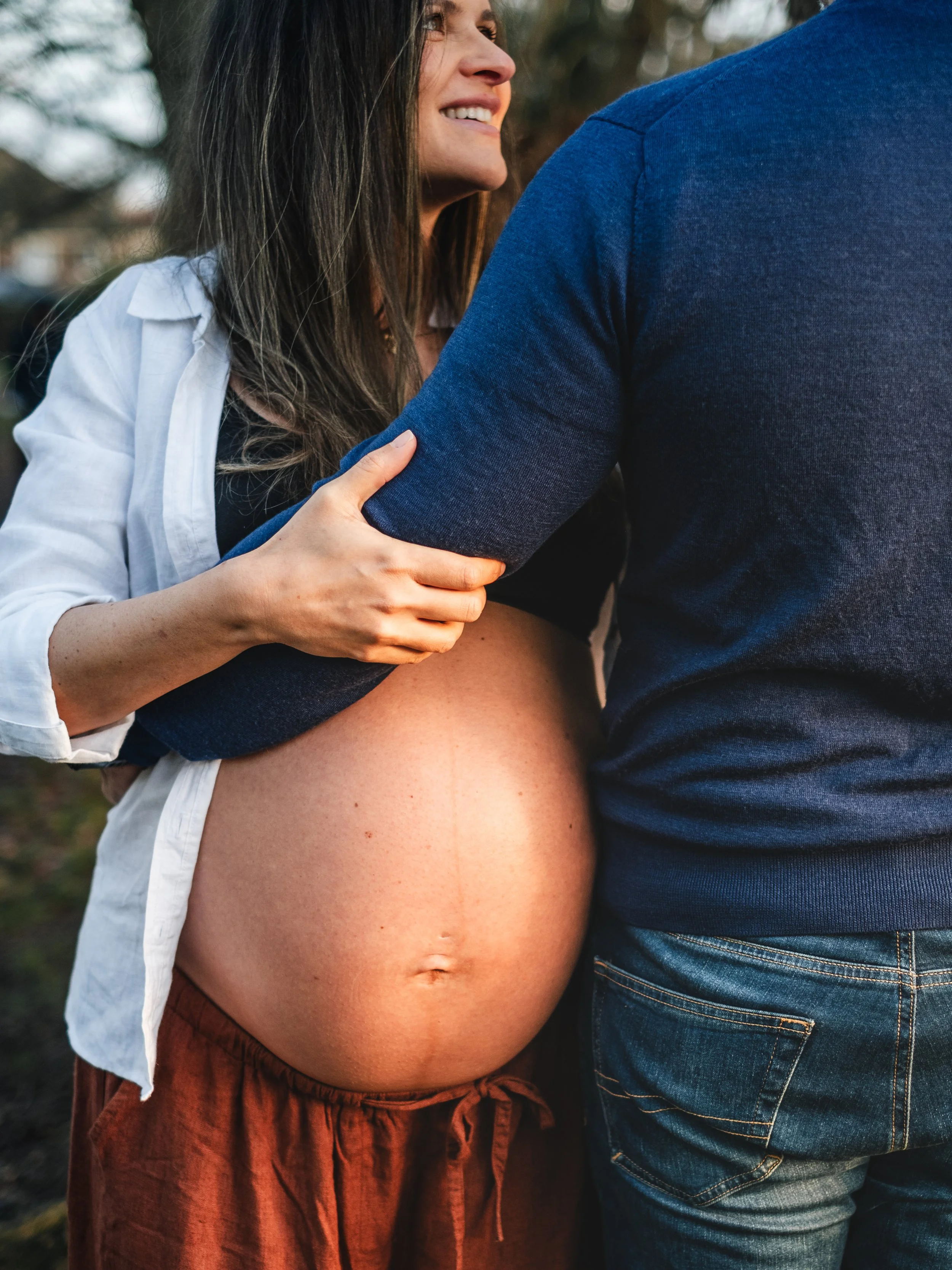 A pregnant woman smiling gently with a man, her hand touching his arm outdoors during daytime.