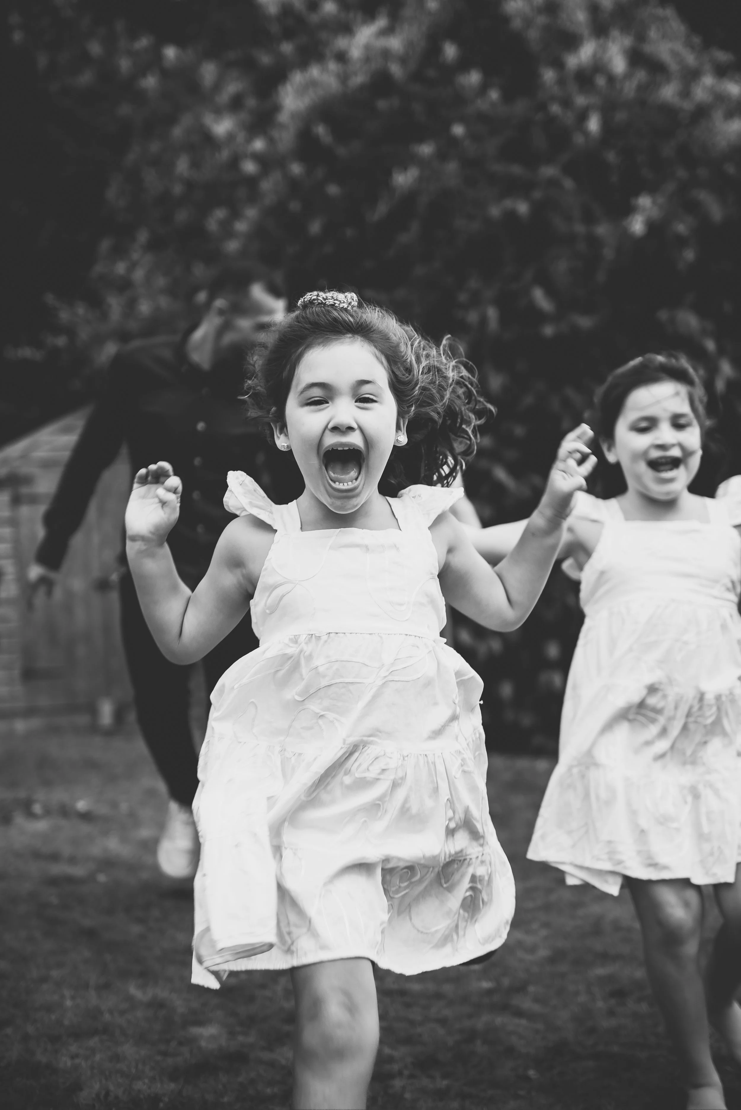 Family Photoshoot with black and white photo of young girls running outdoors, smiling and cheering, in a park or garden setting.
