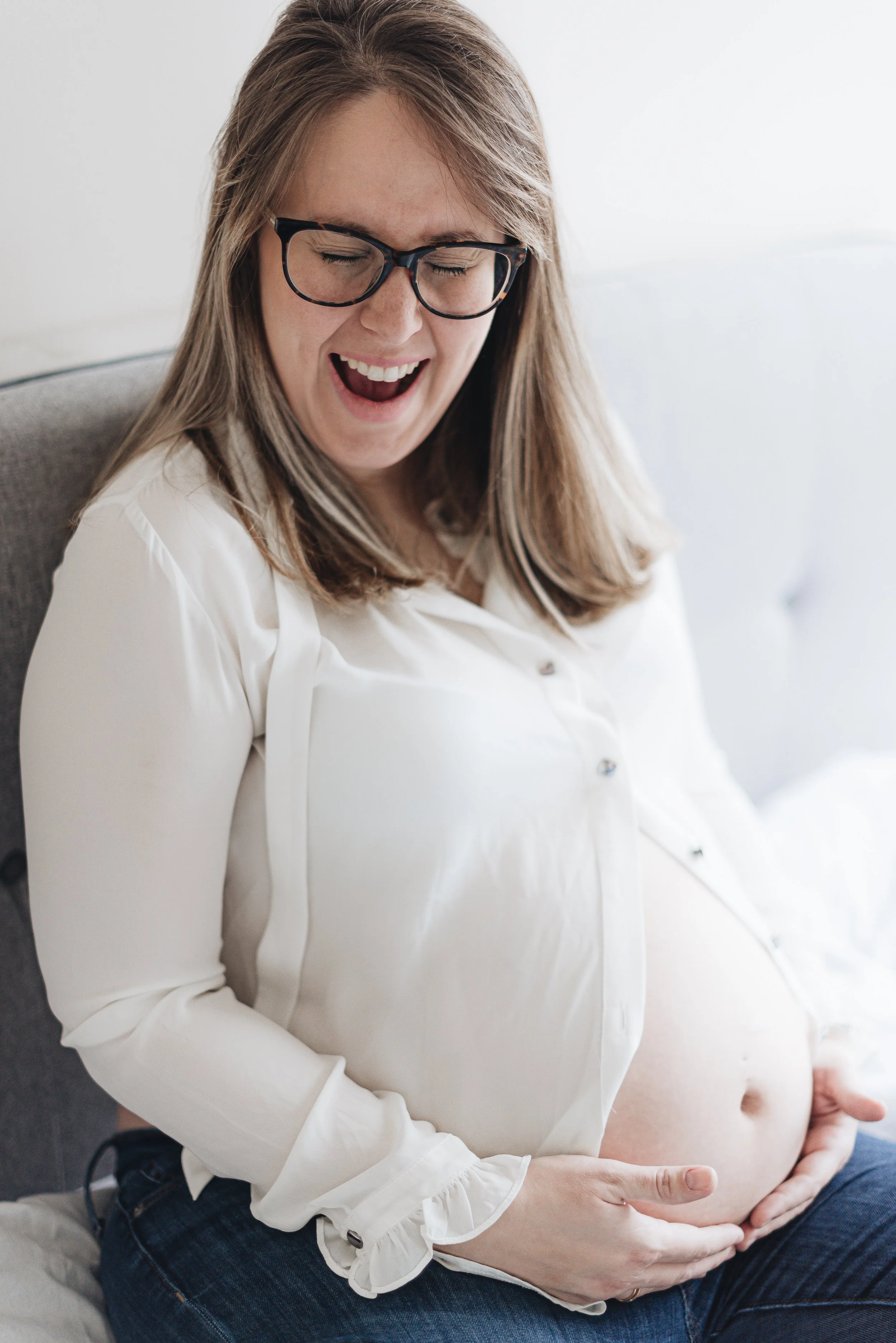 Pregnant woman smiling and holding her belly while sitting on a couch.