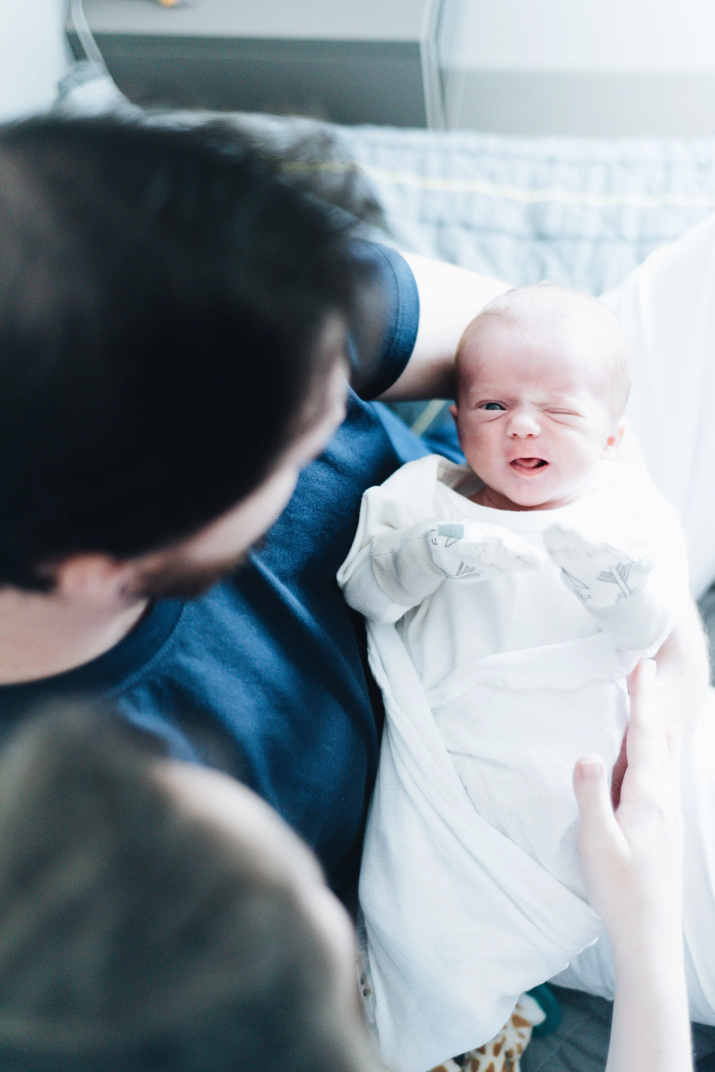 A person holding a newborn baby in a hospital bed, with the baby making a grimace.