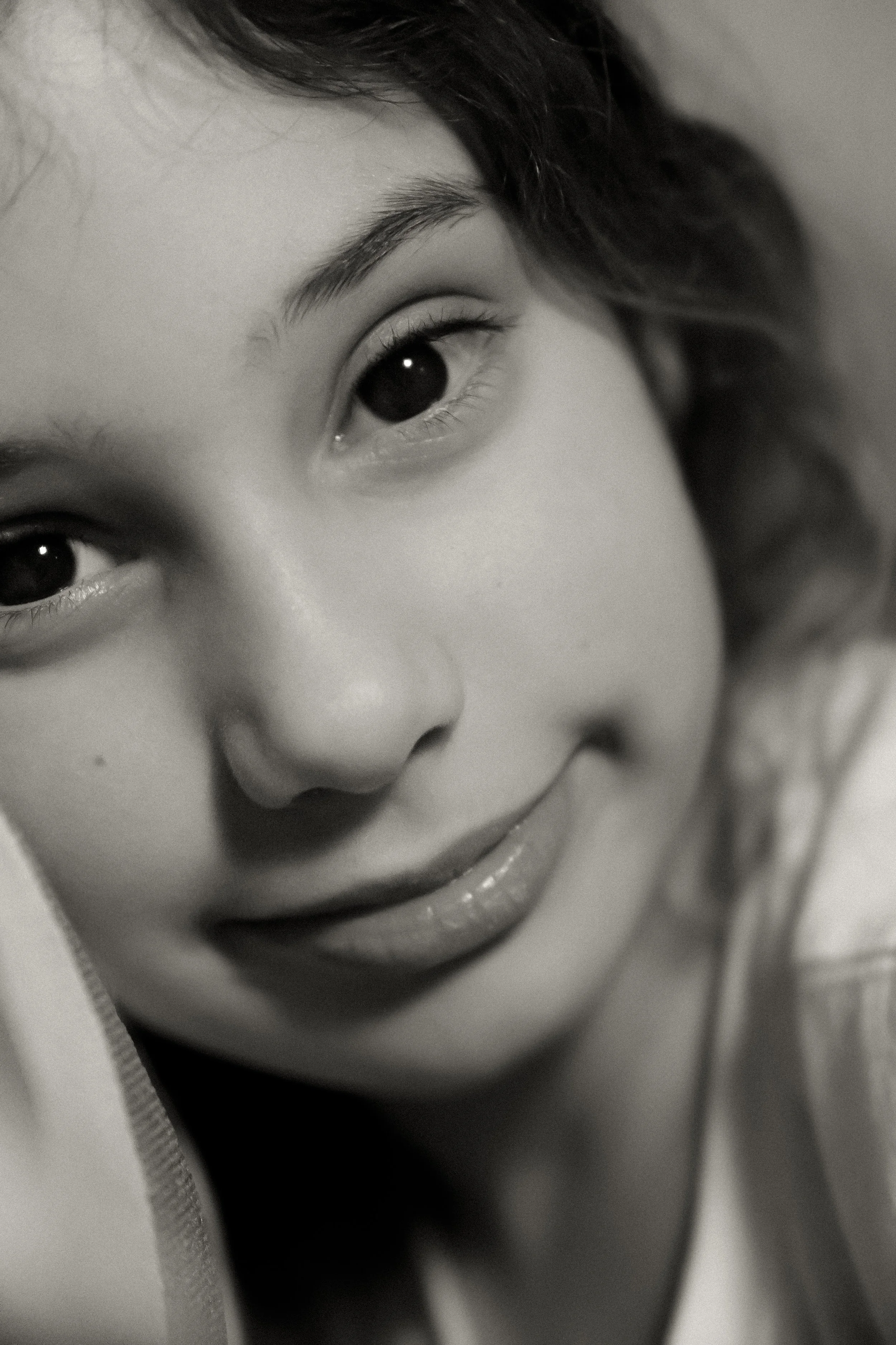 Close-up of a young woman's smiling face in black and white, showing her eyes, nose, and lips.
