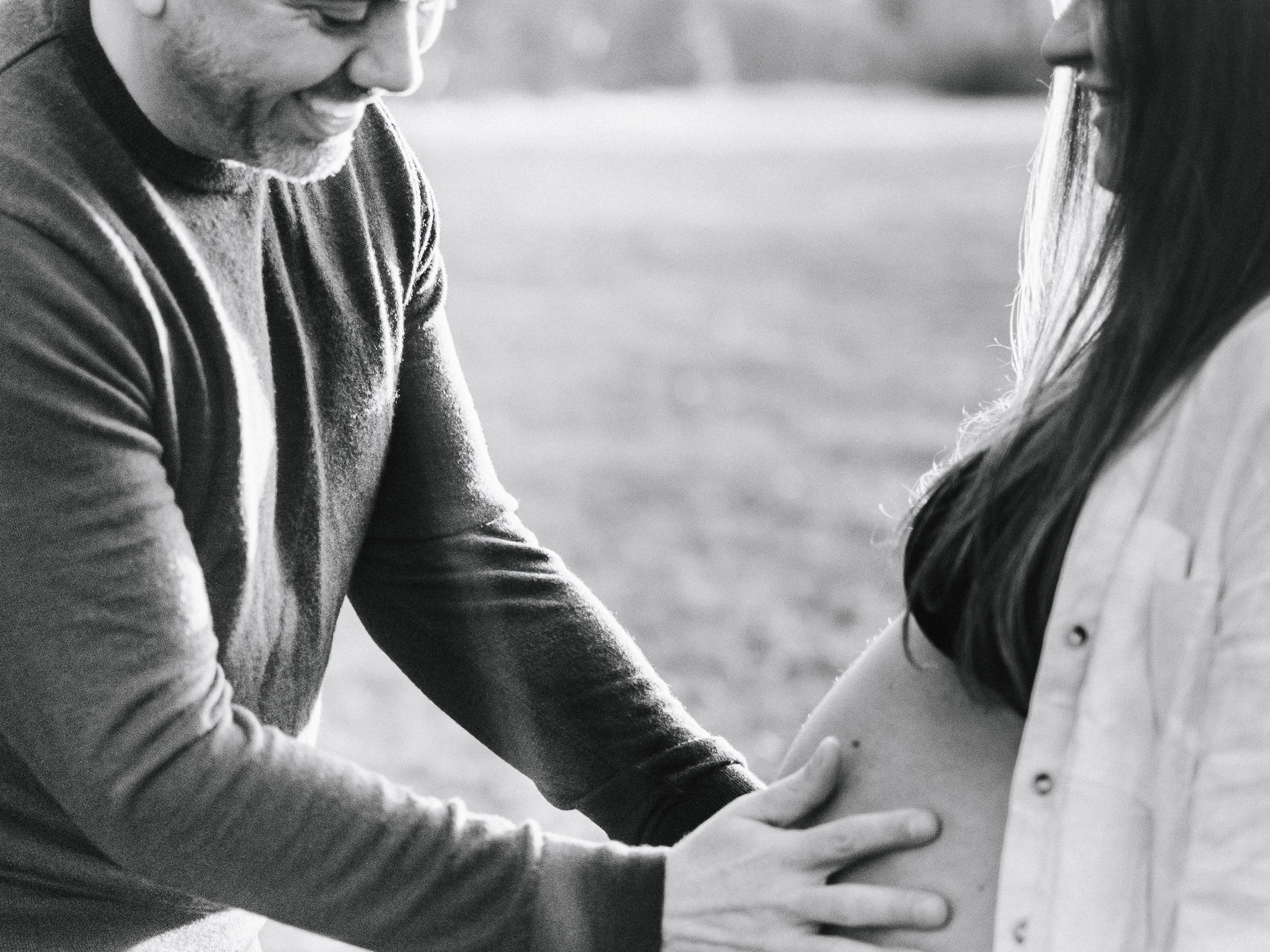 A man smiling and holding a woman's shoulder outside, in black and white.