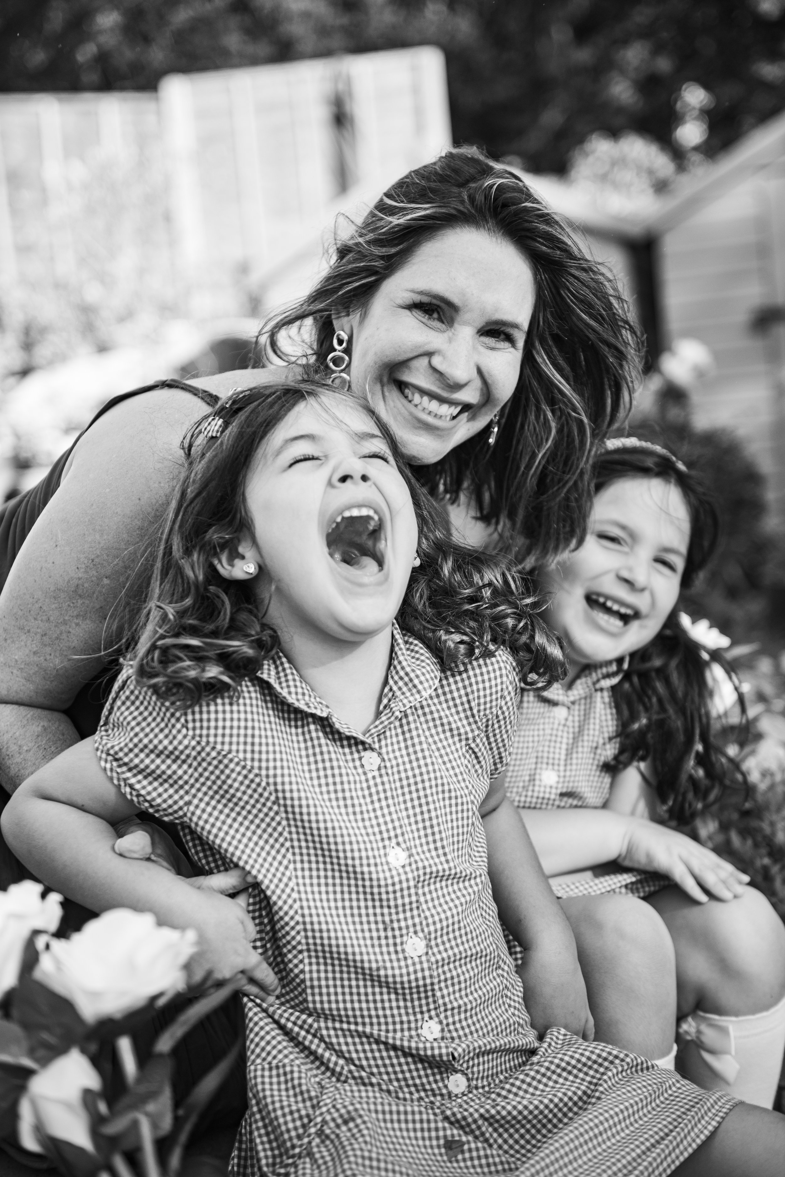 A woman and two young girls smiling and laughing outdoors.
