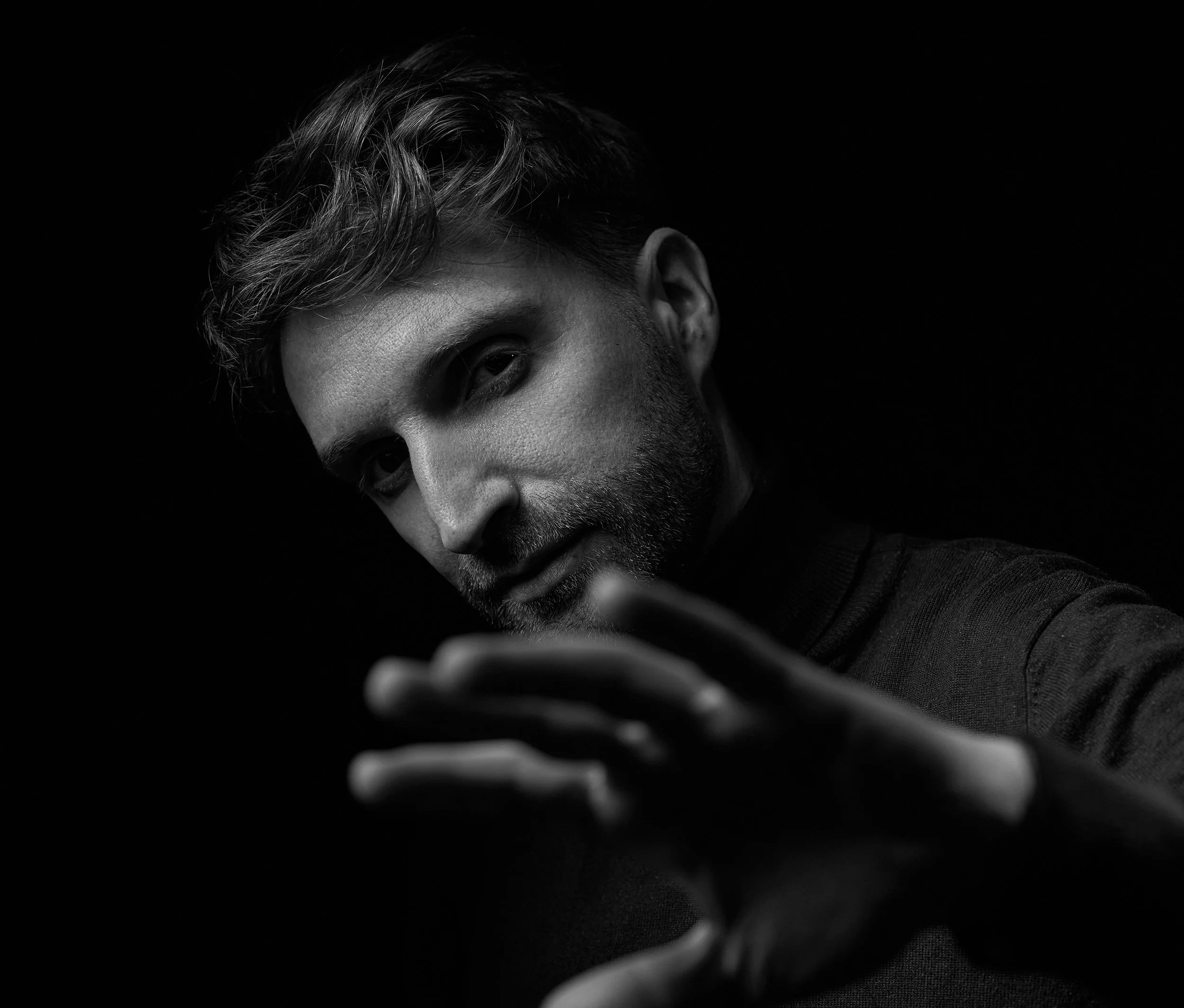 Portret alb-negru in studio Tg.Mures al unui bărbat cu părul coafat și barbă, care privește atent la cameră în timp ce întinde mâna înainte.