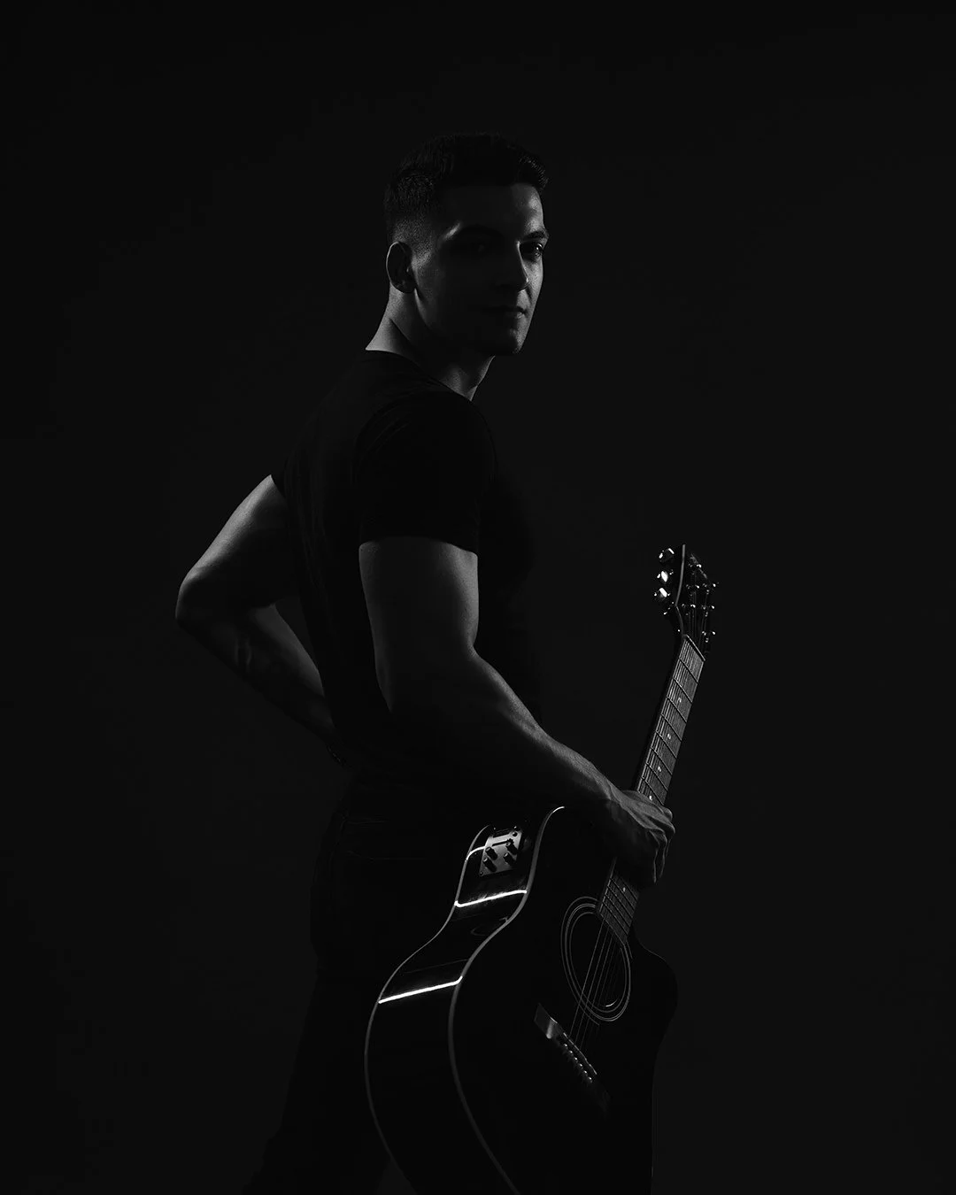 A person holding an acoustic guitar, dark background, low-key lighting.