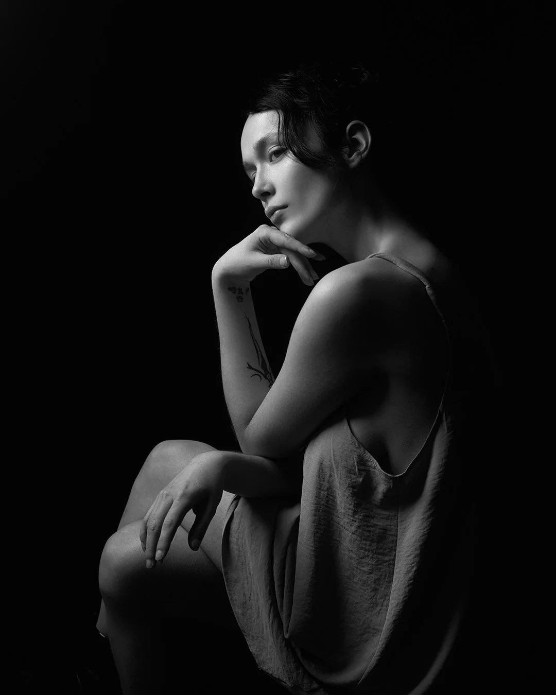 Portret artistic alb-negru al unei femei, realizat în studio, cu lumină dramatică și expresie contemplativă, într-un stil minimalist și cinematic.