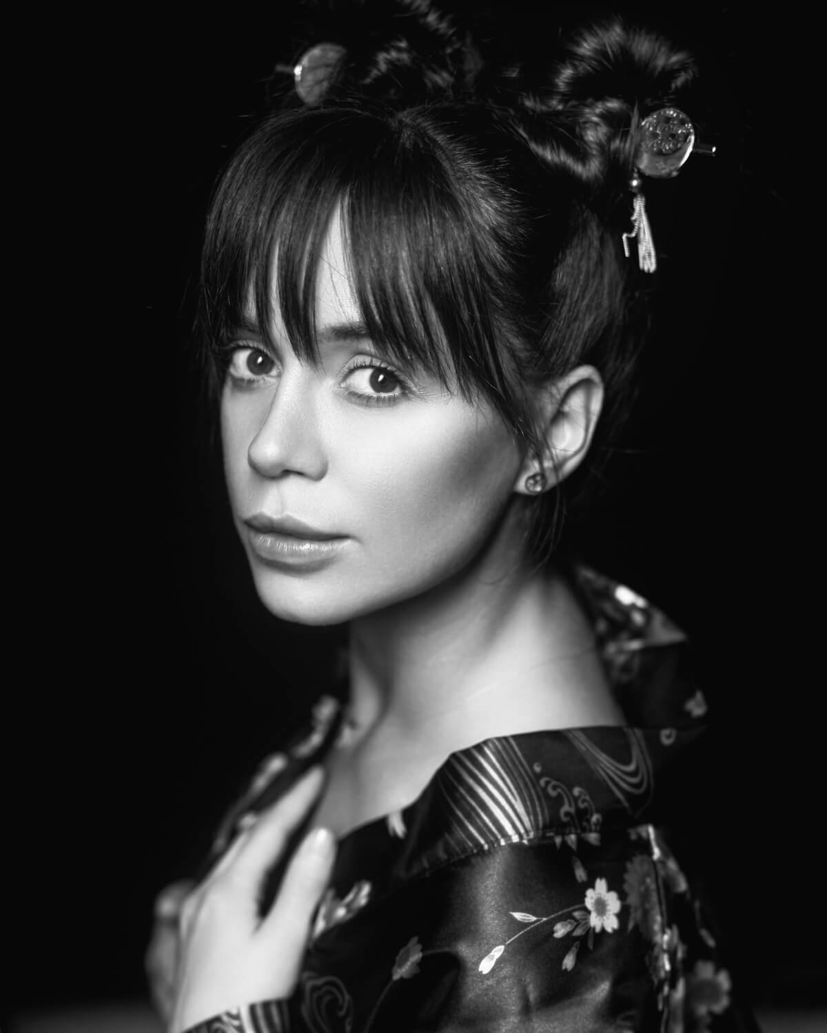 Black and white portrait of a woman with styled hair in an updo, wearing traditional floral clothing, looking at the camera with a gentle expression.