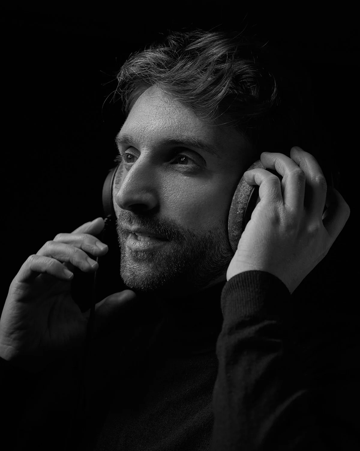 A man with a beard and wavy hair wearing headphones, looking thoughtfully.