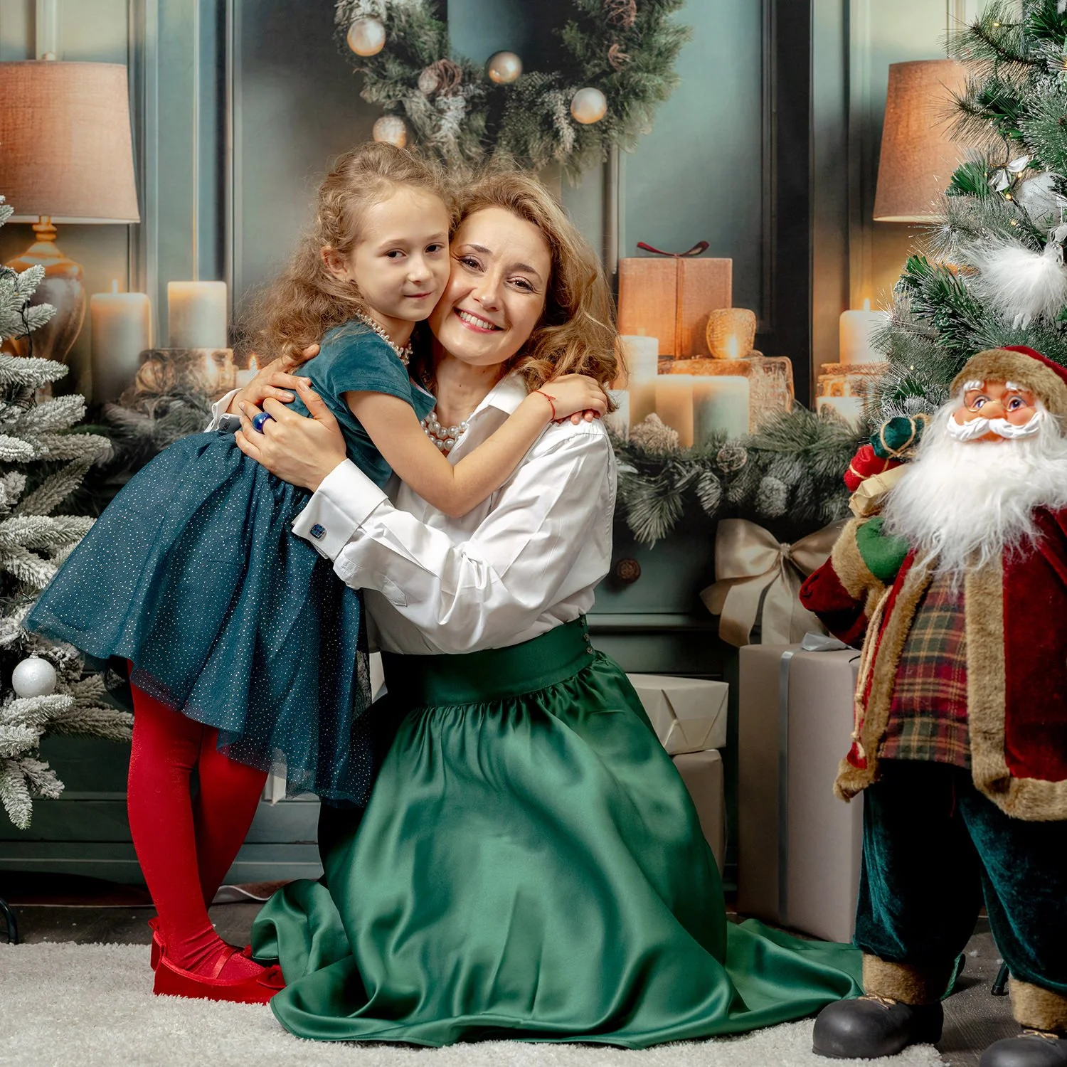 A woman and a young girl hugging and smiling in a festive Christmas setting with decorated trees, candles, and Santa Claus figure in the background.