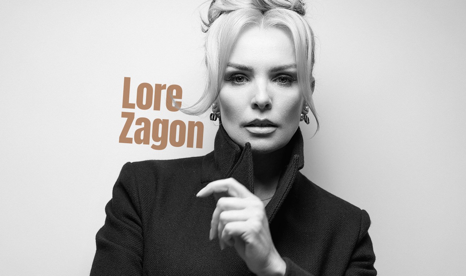 Fotograf Tg Mures - Fotografie alb-negru a unei femei cu părul blond, purtând cercei și o jachetă închisă la culoare cu guler înalt, stând lângă un perete simplu. Textul „Lore Zagon” este scris cu culoarea cafenie în partea stângă a imaginii.