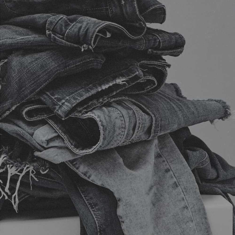 Stacked pile of dark and light denim jeans and shorts.