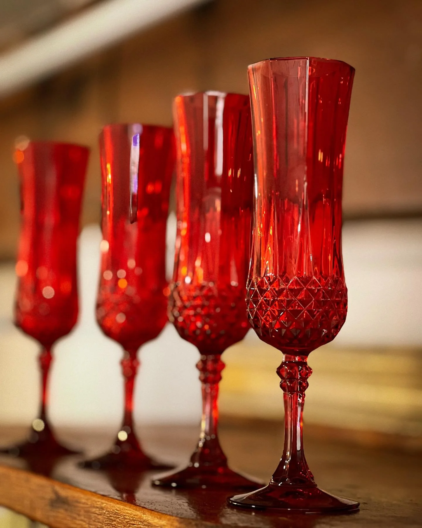Four tall red crystal champagne flutes with textured surfaces, arranged in a line on a wooden surface.