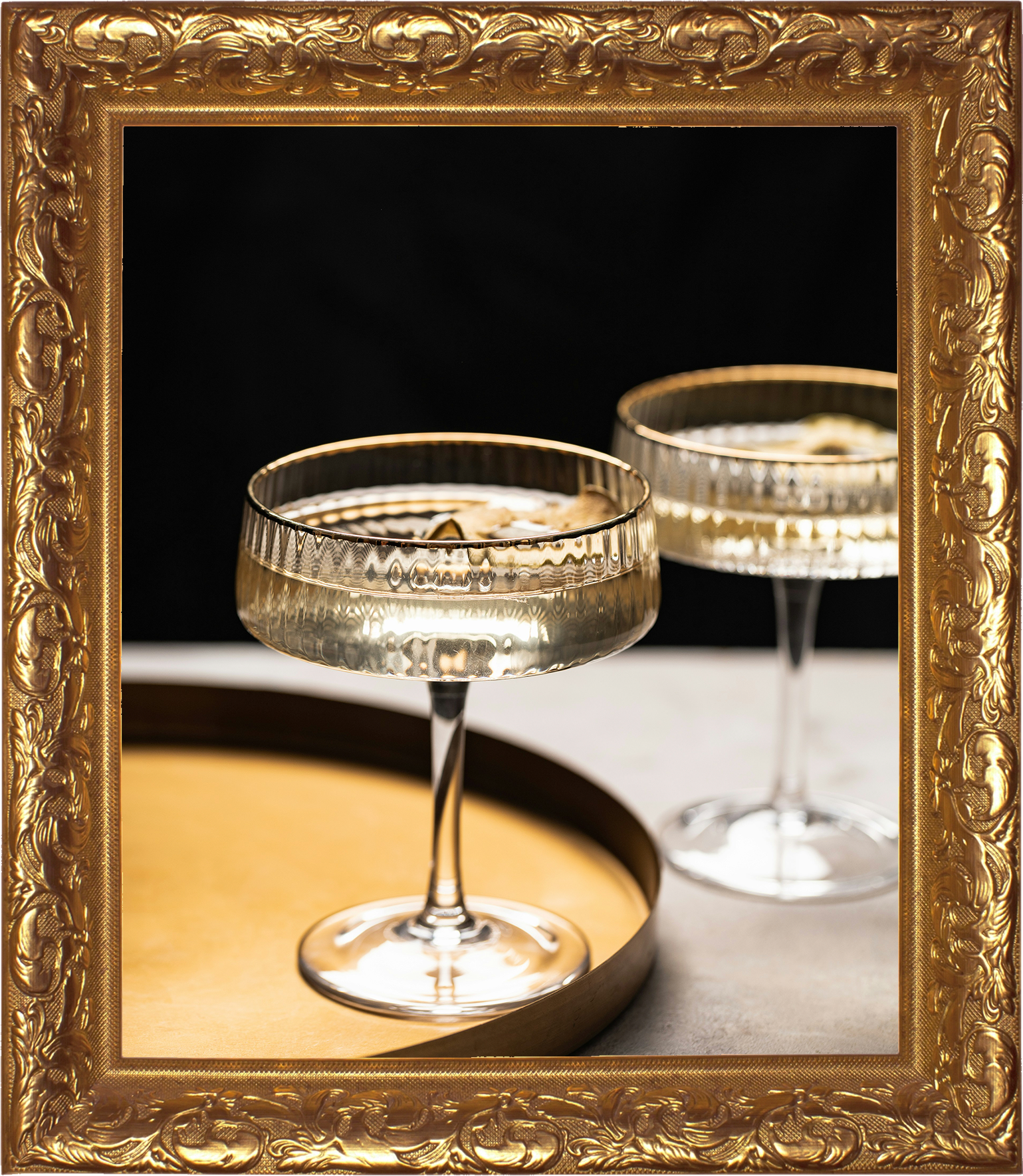 Born Again Consignment Parlor. Printers Row. Two vintage cocktail glasses with textured patterns on the rims, placed on a tray with a gold border frame around the image.