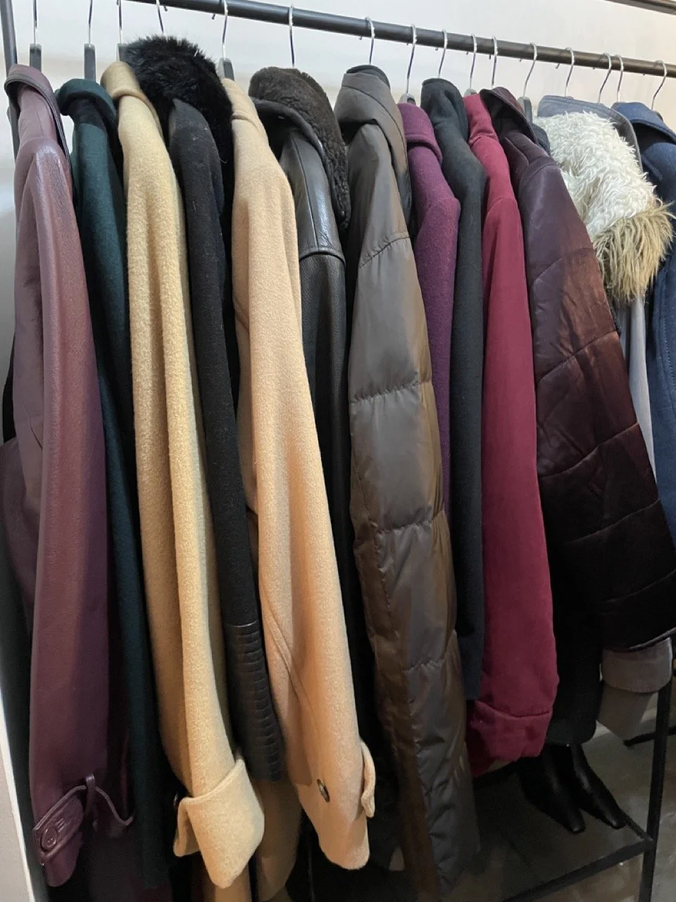 A clothing rack with various winter jackets and coats in different colors and styles, including leather, puffer, and fleece.