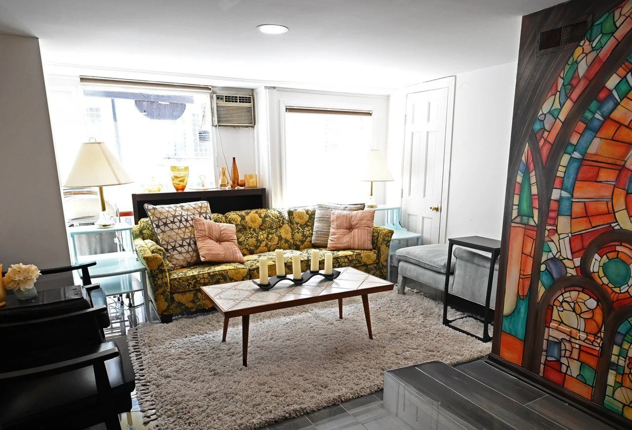 Event space at Born Again Consignment Parlor. Printers Row. Large windows with blinds, decorative vases on a black shelf, and colorful stained glass artwork on the right.