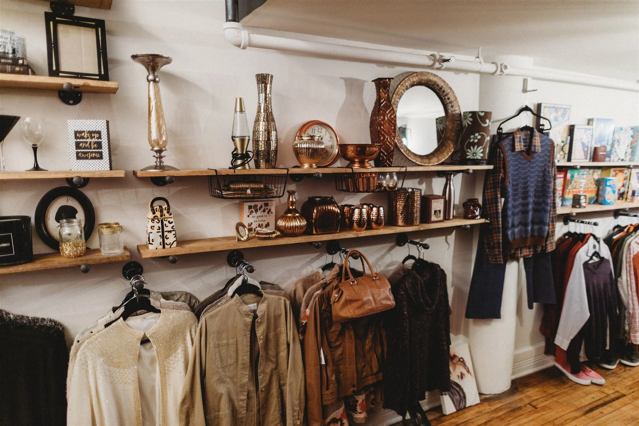 Born Again Consignment Parlor. Printers Row. Interior of a thrift store with wooden shelves displaying decorative items, mirrors, and vases, along with clothing racks holding jackets, shirts, and handbags.
