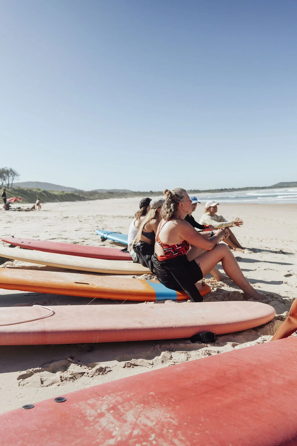 Group of people sitting on paddleboards on the sandy beach, facing the ocean with surfboards laid on the sand.