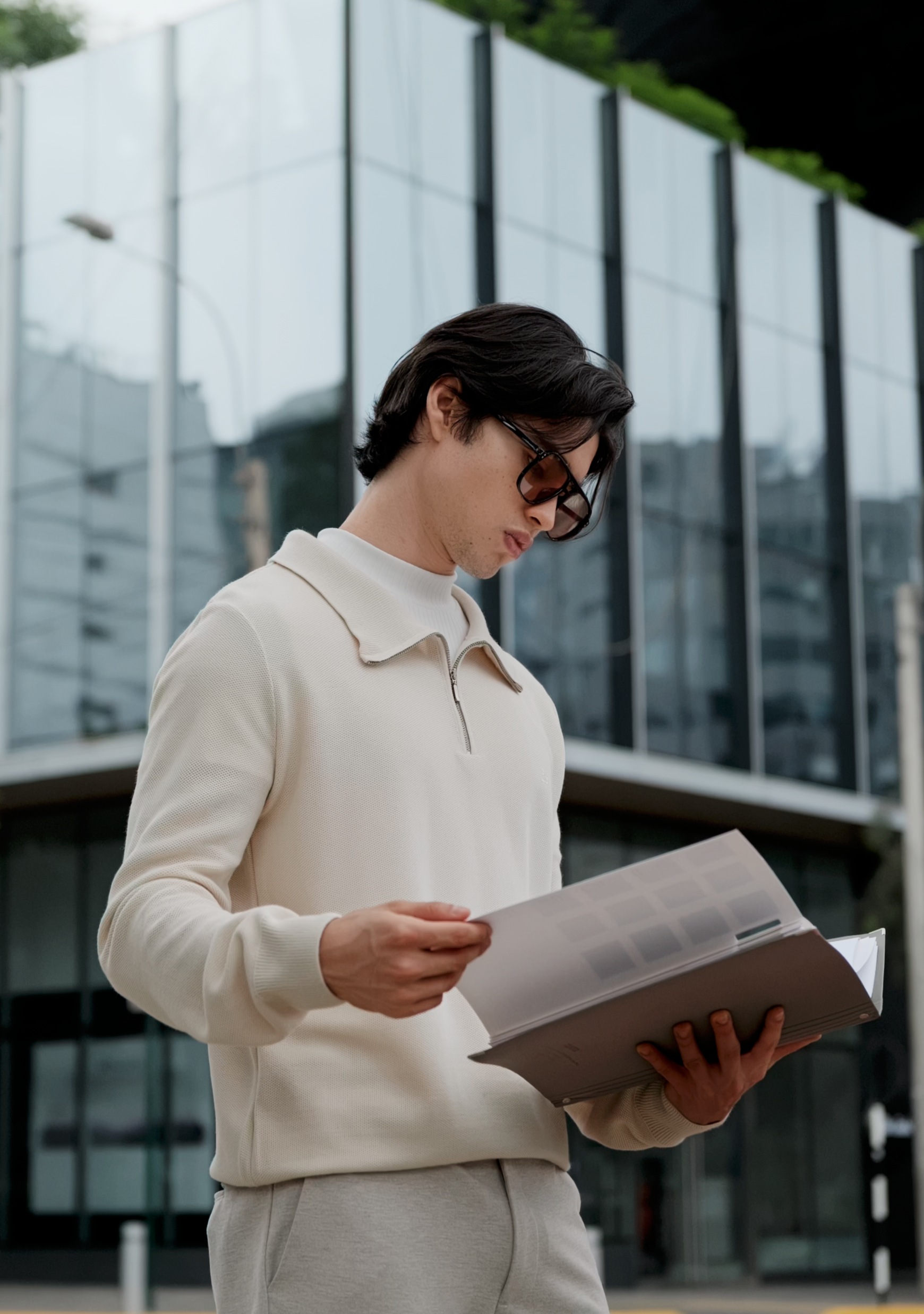Persona leyendo un documento frente a un edificio moderno de vidrio.